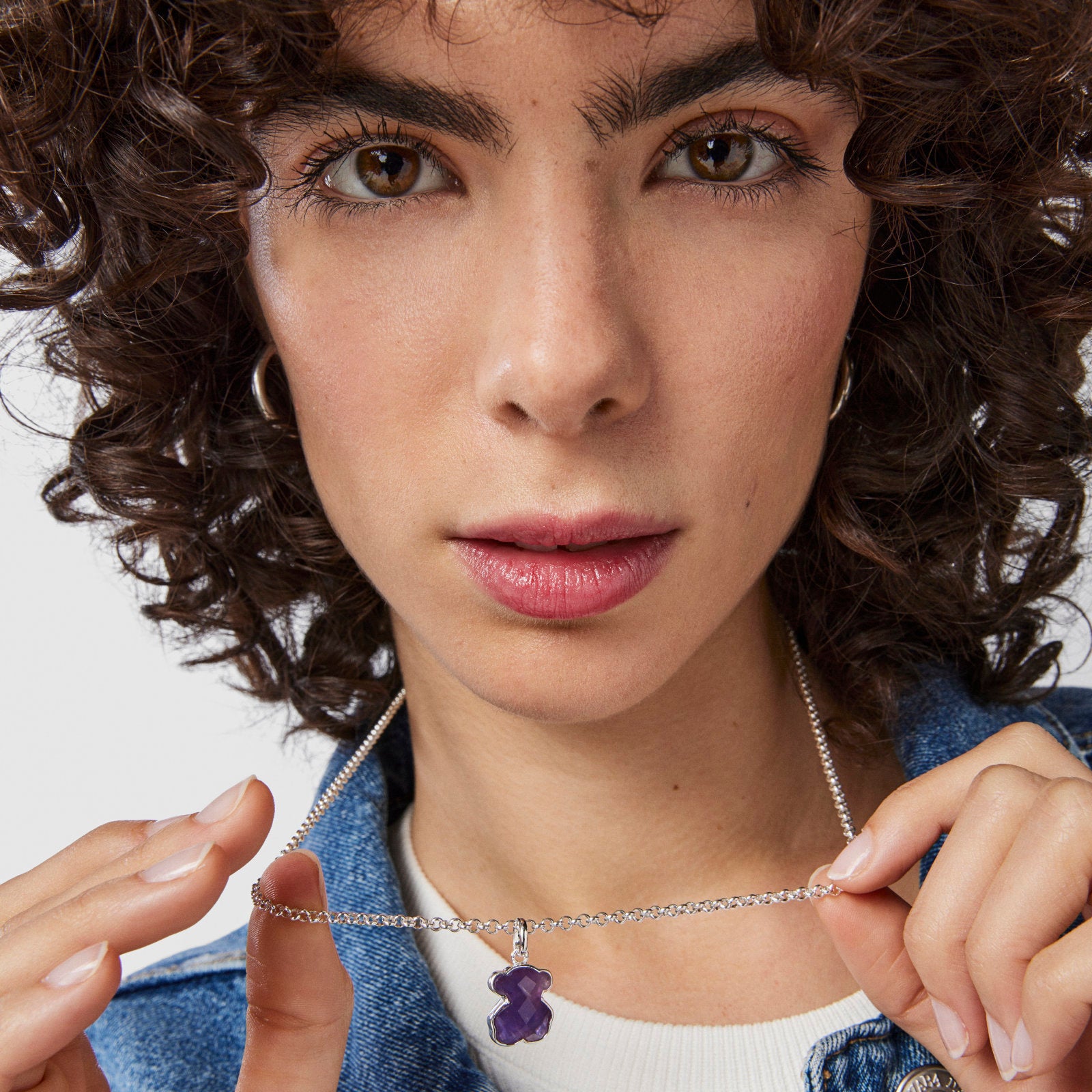 אישה עם שיער מתולתל מחזיקה שרשרת כסף עם תליון סגול בצורת דובי