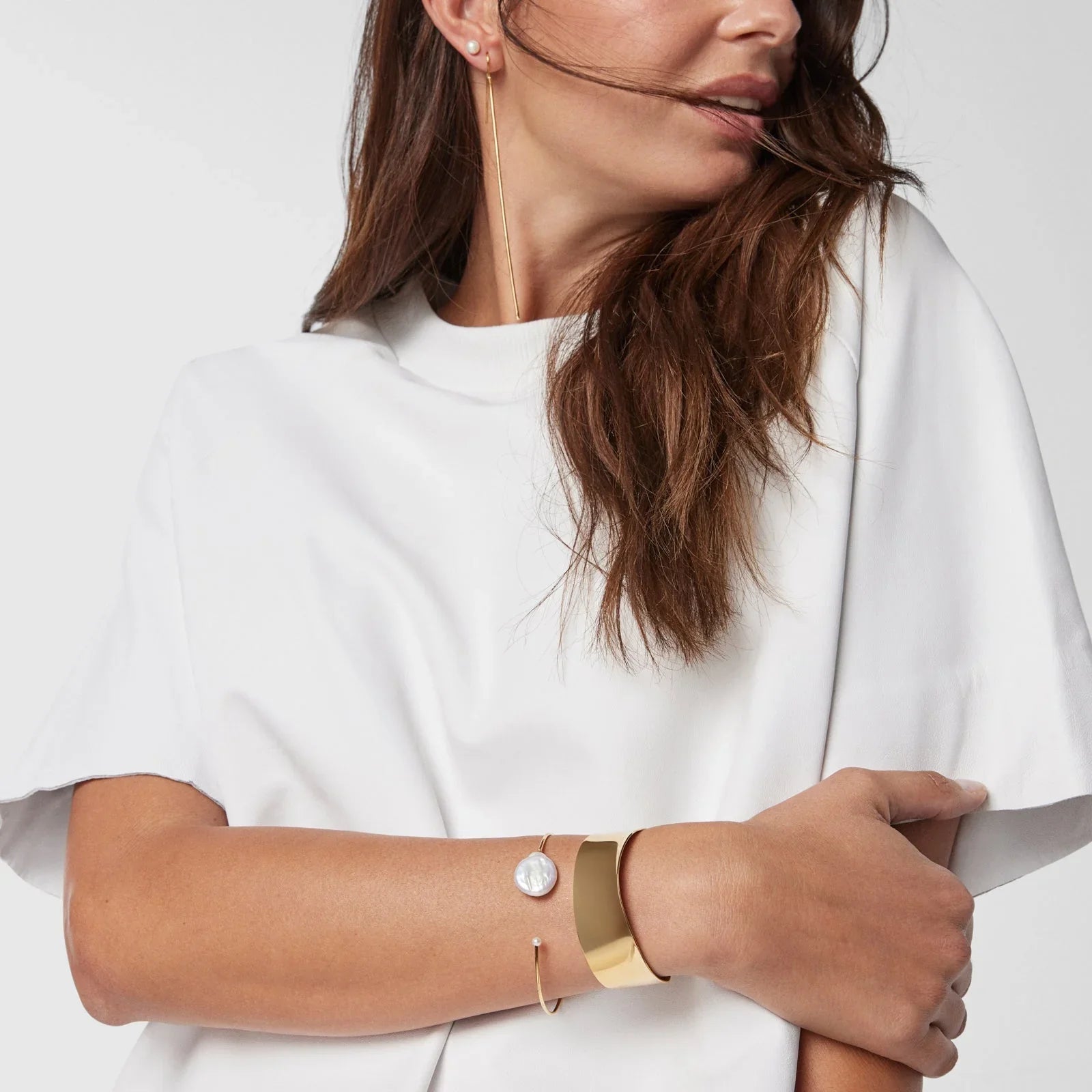 אישה לובשת חולצה לבנה עם תכשיטי זהב יוקרתיים, צמידים ועגילים, CHOZEN מותגים מובילים