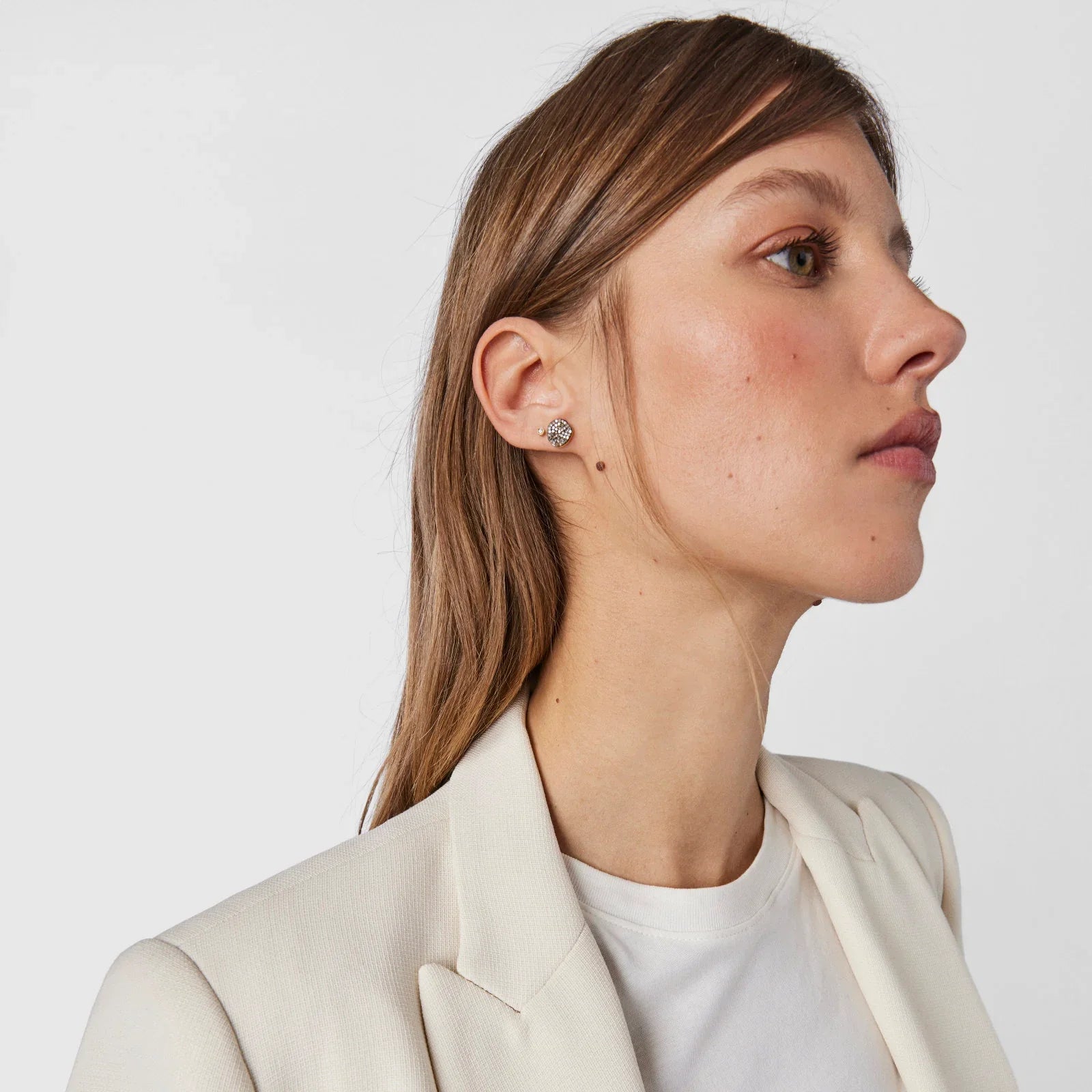 אישה עם עגילי יהלום קטנים, לבושה בלייזר לבן, ממותגי CHOZEN