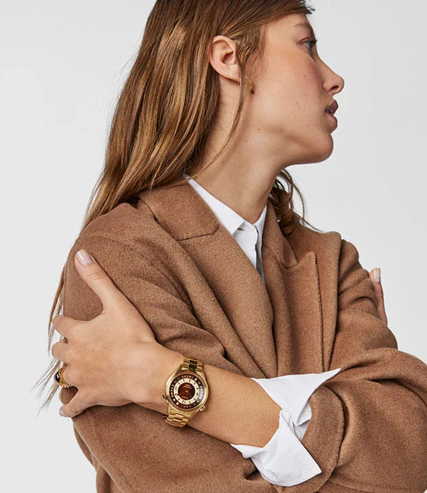 אישה עם מעיל בז' עונדת שעון יוקרתי זהב, אופנה מבית CHOZEN אלפא