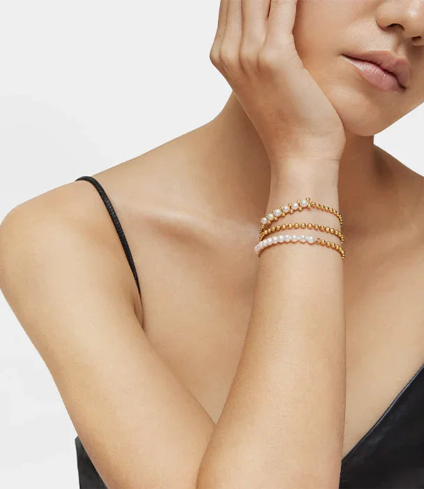 דוגמנית עם צמידי פנינה וזהב קלאסיים על רקע לבן, תכשיטי CHOZEN מבית קבוצת אלפא