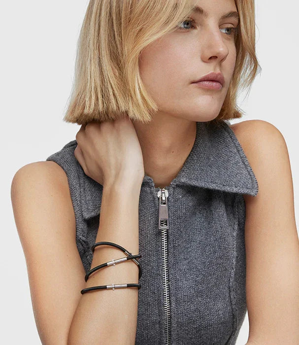 אישה עם שיער בלונד קצר, לובשת גופיית צמר אפורה עם רוכסן וצמידי CHOZEN שחורים על היד