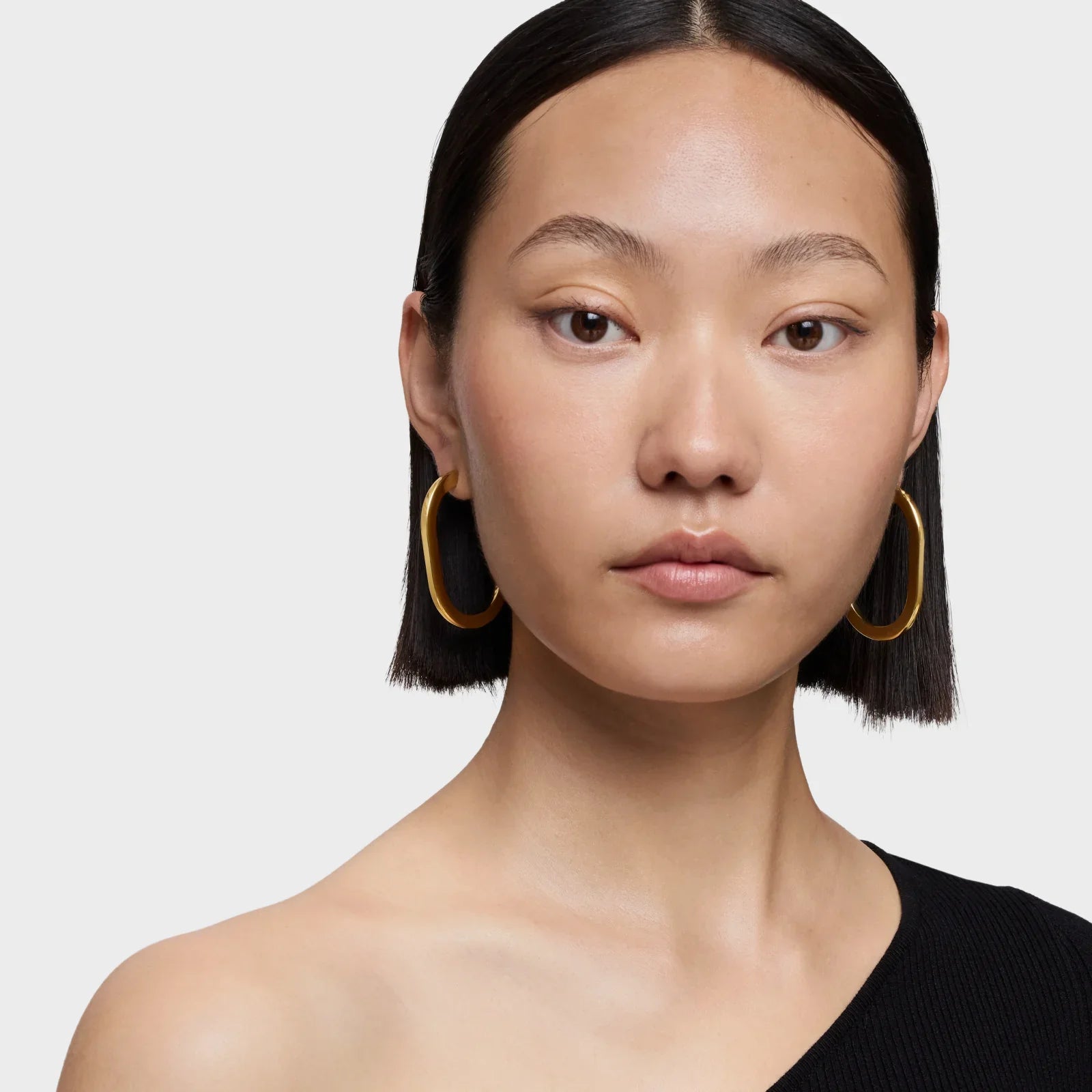 אישה עם שיער כהה קצר עונדת עגילי חישוק זהב גדולים, צילום תקריב לאתר CHOZEN