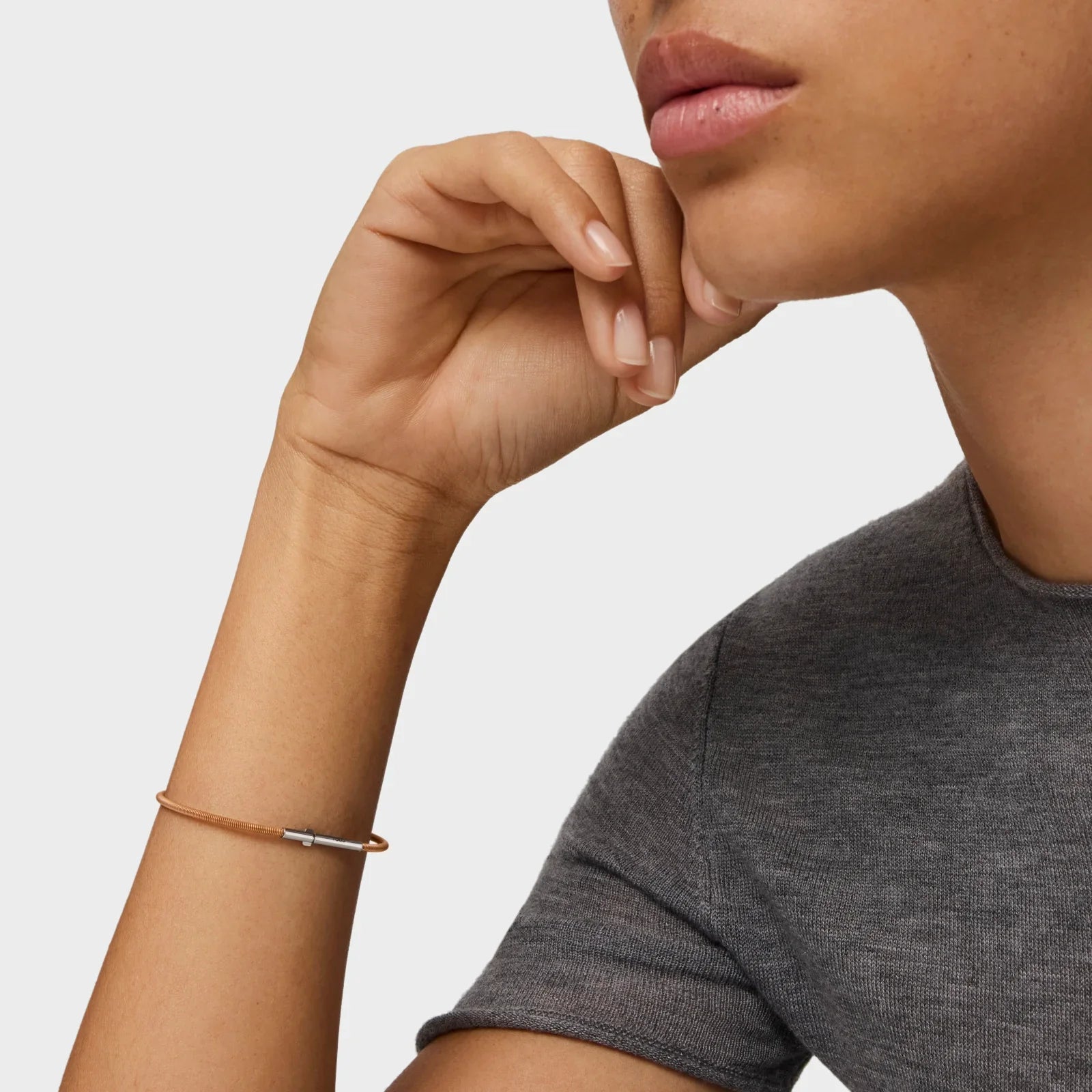 צמיד דק מזהב על יד של אישה, חולצה אפורה, קולקציית תכשיטים CHOZEN