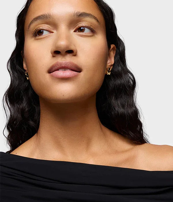 אישה עם שיער כהה גלי עונדת עגילי זהב, רקע לבן, אופנה CHOZEN