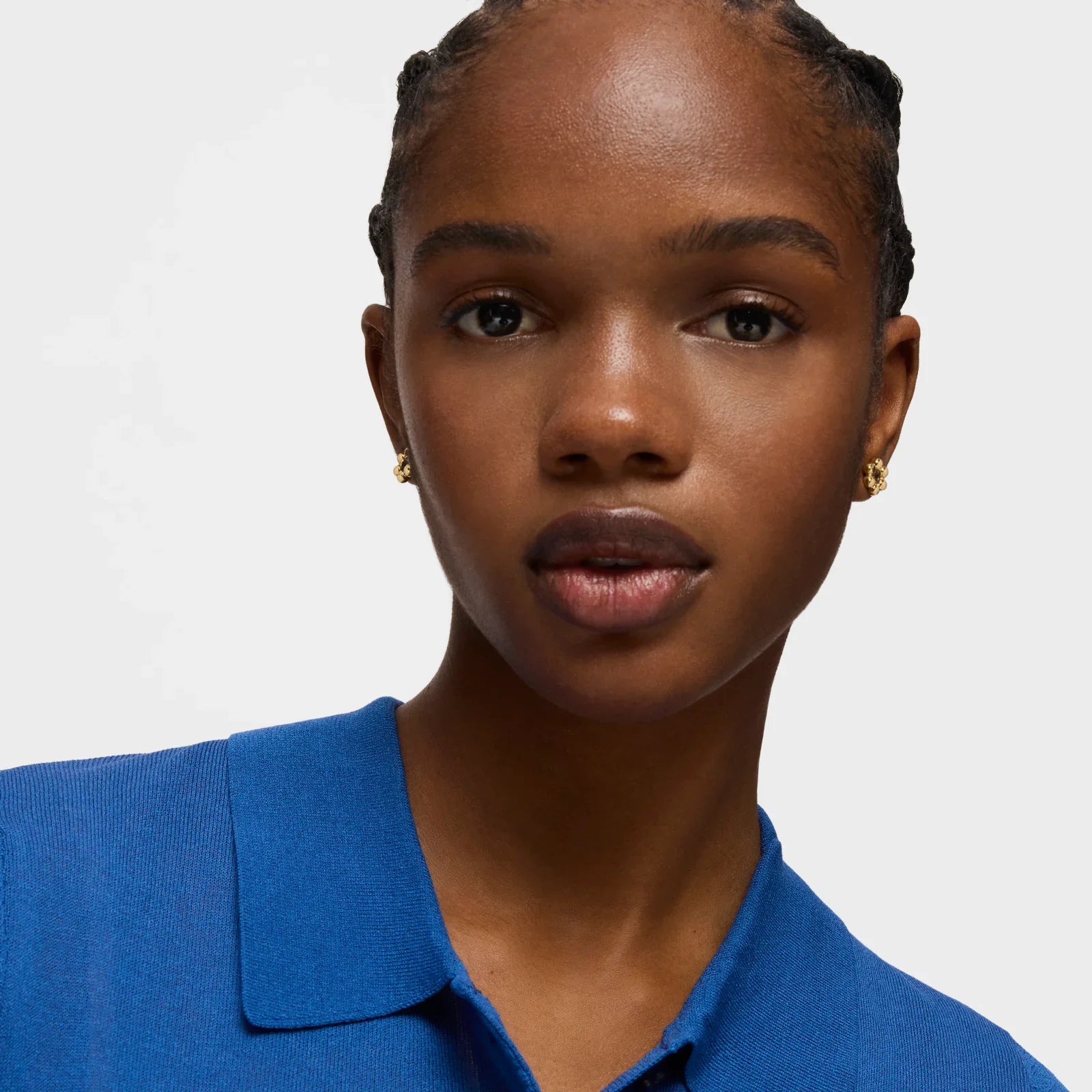 דוגמנית עם עגילים זהובים בלוק קז'ואל, לובשת חולצה כחולה, צולמה ל-CHOZEN מותגים מובילים