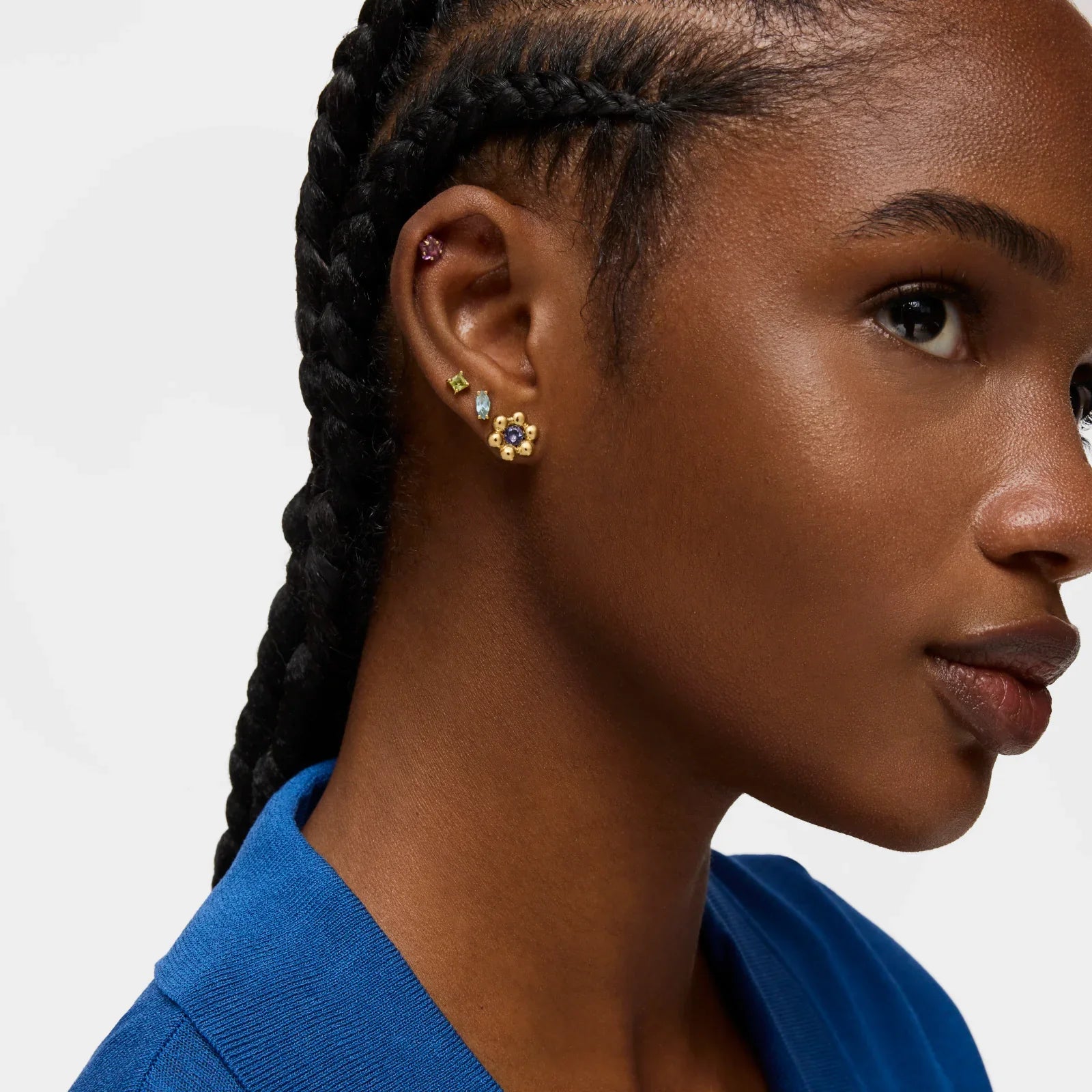 אישה עם צמות עונדת עגילי זהב משובצים אבני חן צבעוניות, צילומי תקריב, CHOZEN מותגים מובילים