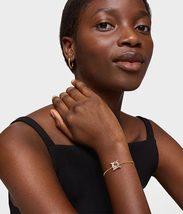 אישה לובשת שמלת ערב שחורה ותכשיטי זהב אופנתיים, כולל צמיד, מטעם CHOZEN