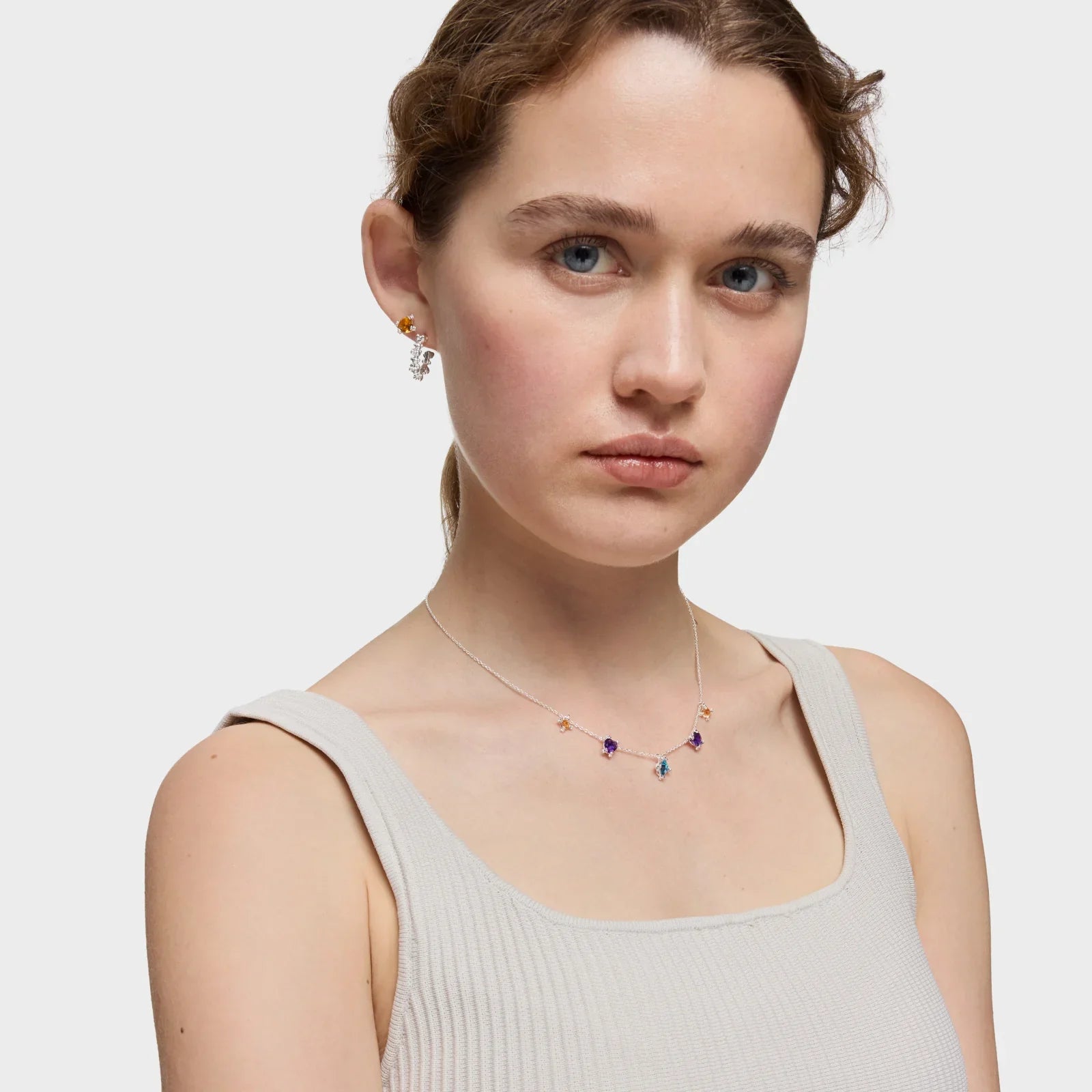 אישה צעירה עונדת שרשרת כסף עדינה עם תליונים צבעוניים ועגילים, צילום אופנה מבית CHOZEN