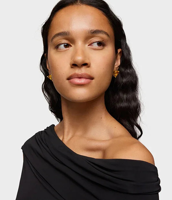 אישה עם שיער שחור גלי, עונדת עגילי זהב, לובשת שמלה שחורה אלגנטית, צילום סטודיו ממותג CHOZEN