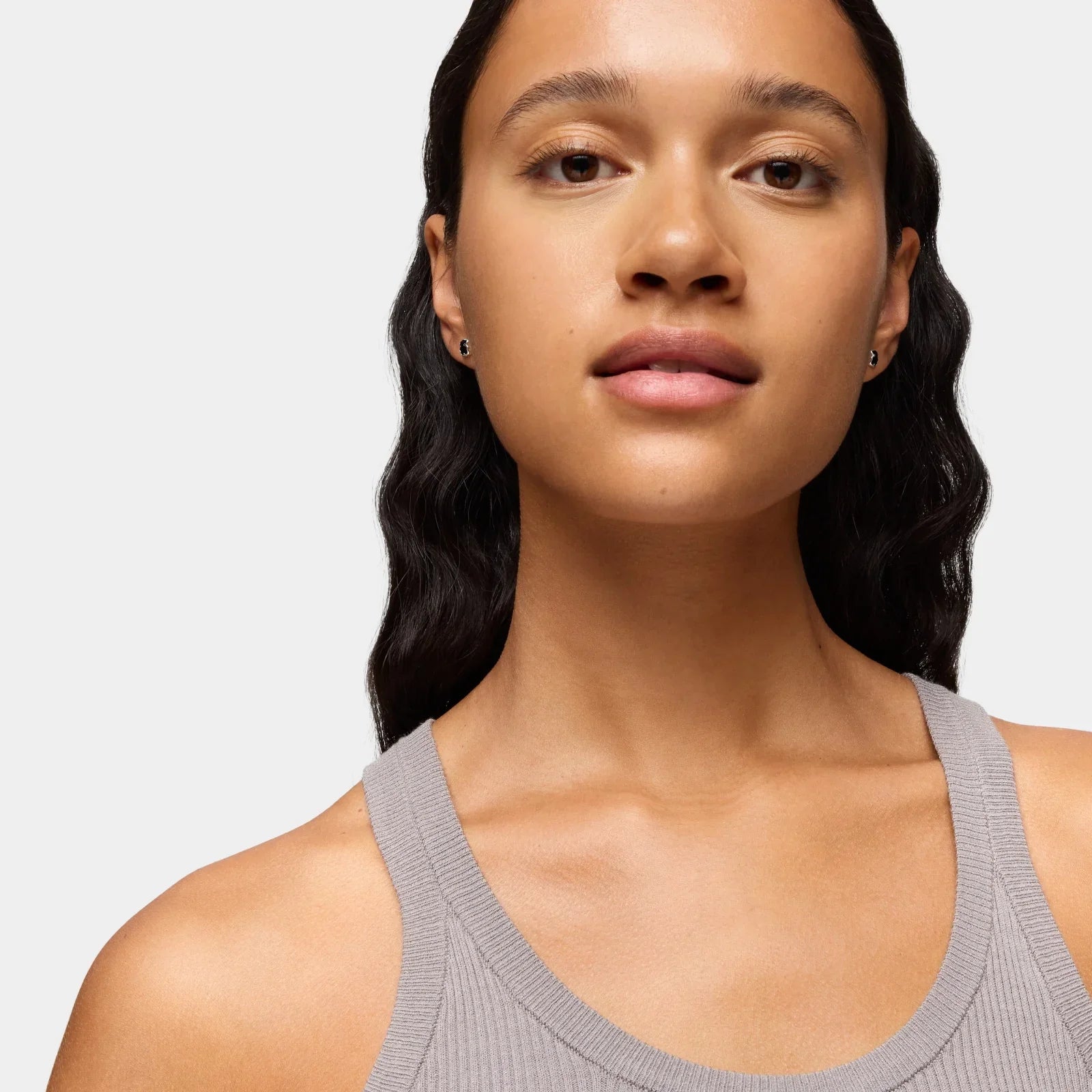 אישה עם שיער כהה גלי לובשת גופיית ריב אפורה, צילום תקריב לפרסום CHOZEN