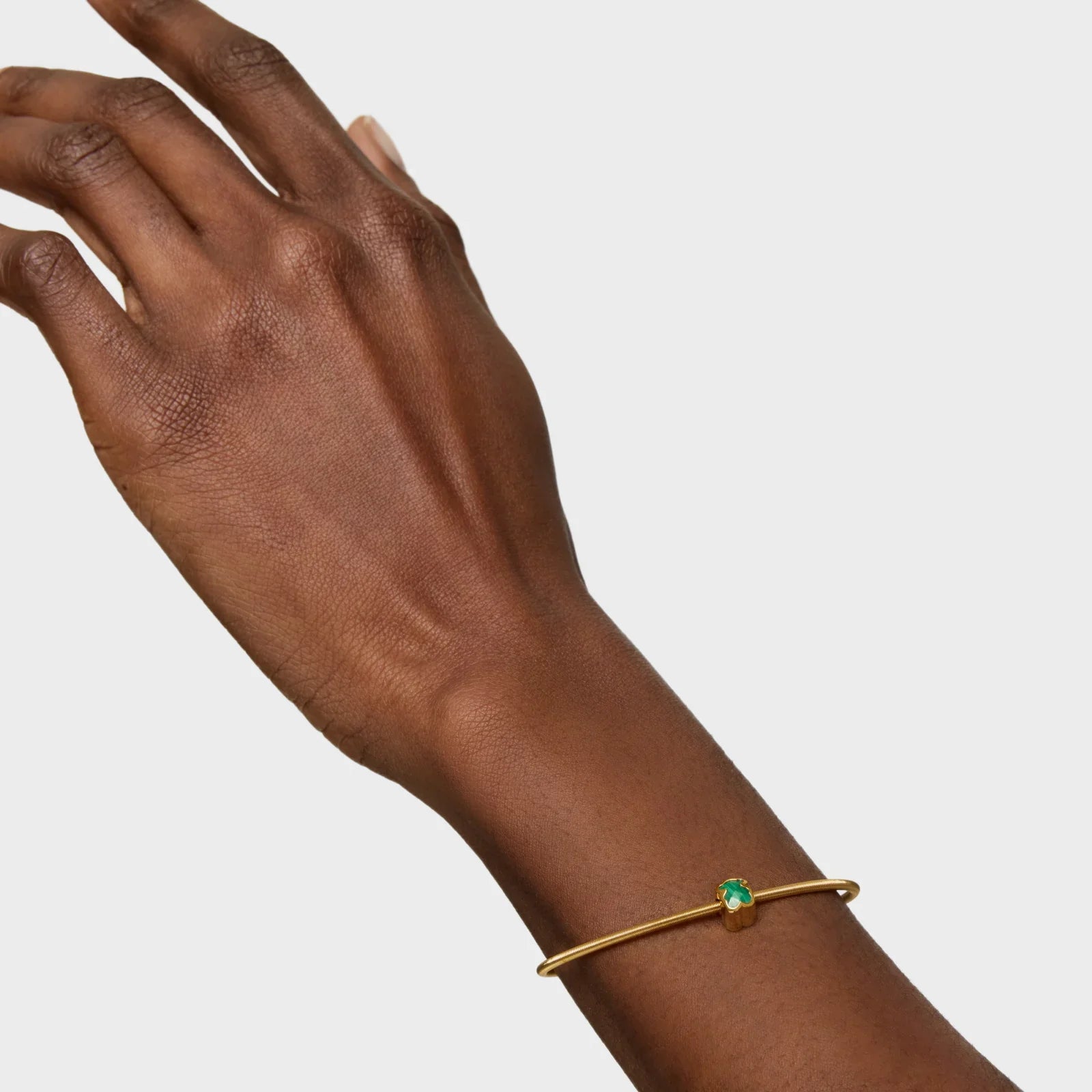 יד עונדת צמיד זהב דק עם אבן ירוקה, תכשיט יוקרתי מבית CHOZEN
