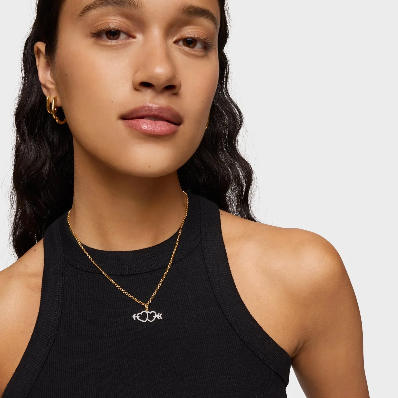 דוגמנית עם שרשרת זהב עדינה בעיצוב לב, עגילי זהב וטופ שחור מבית CHOZEN