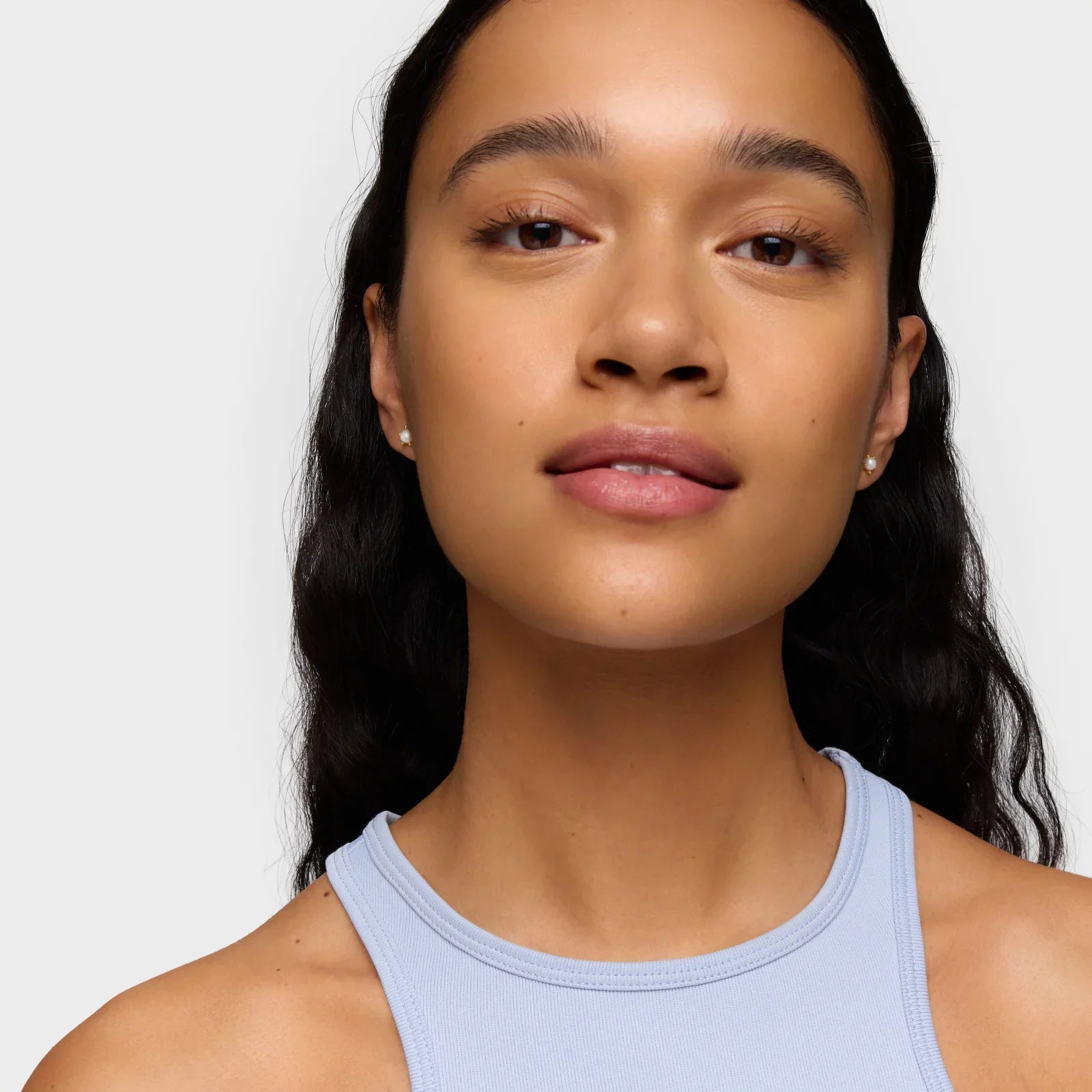 דיוקן אישה צעירה עם שיער כהה גלי, עגילים עדינים וגופיית ספורט, רקע לבן, CHOZEN מותגים מובילים