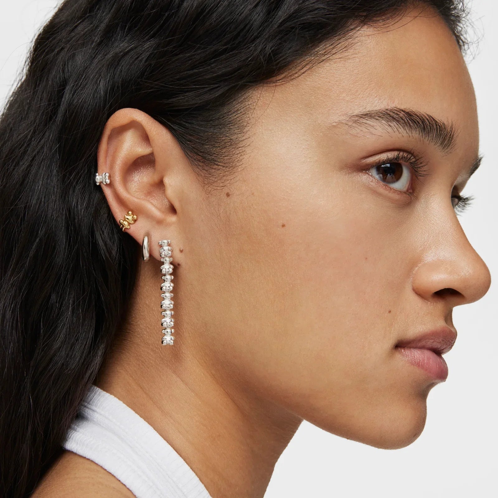 אישה עם עגילי כסף וזהב טרנדיים ליד CHOZEN, תקריב על אוזן עם תכשיטים מעוצבים