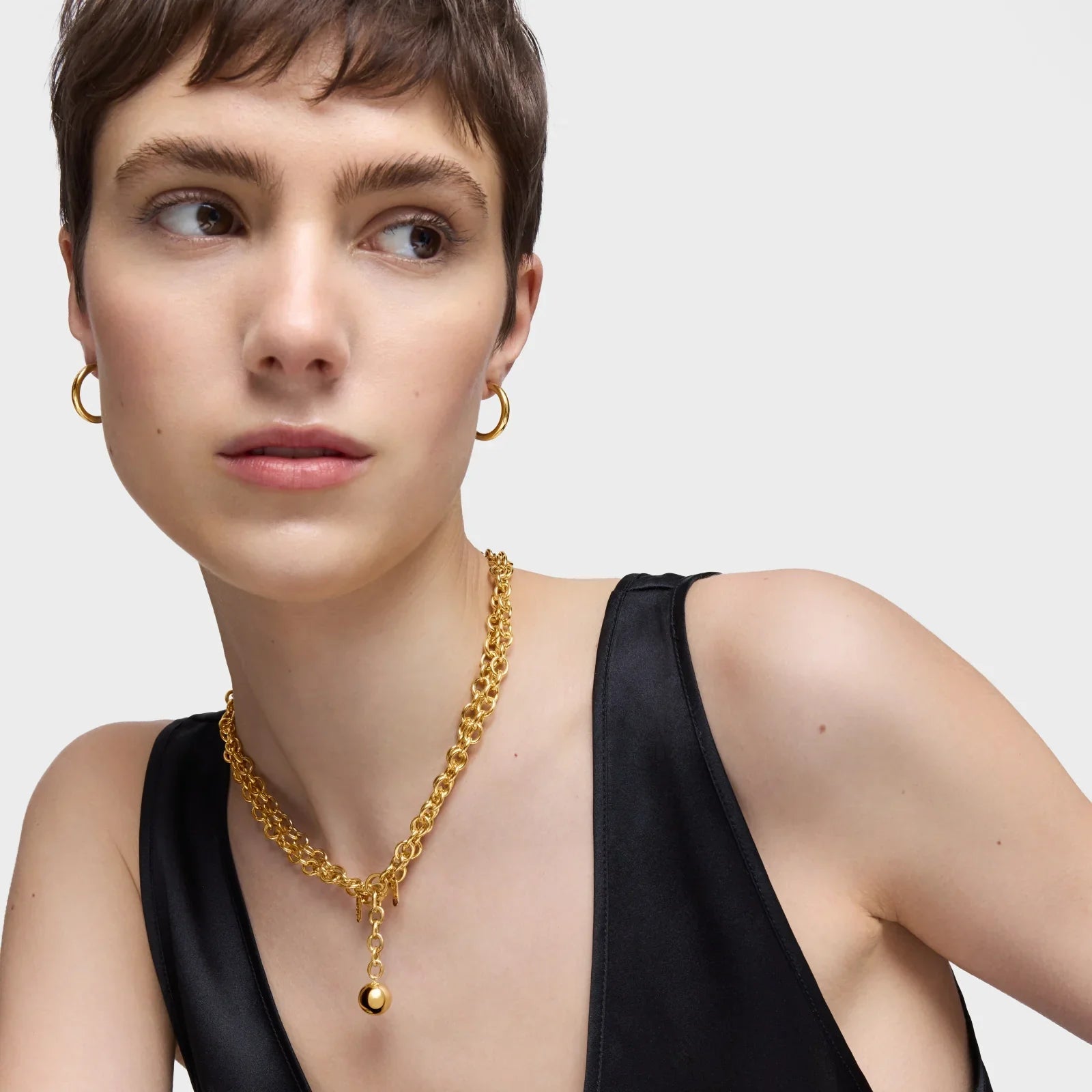 אישה עם שיער קצר עונדת שרשרת זהב ועגילי חישוק זהב, רקע לבן, צילום תדמית CHOZEN