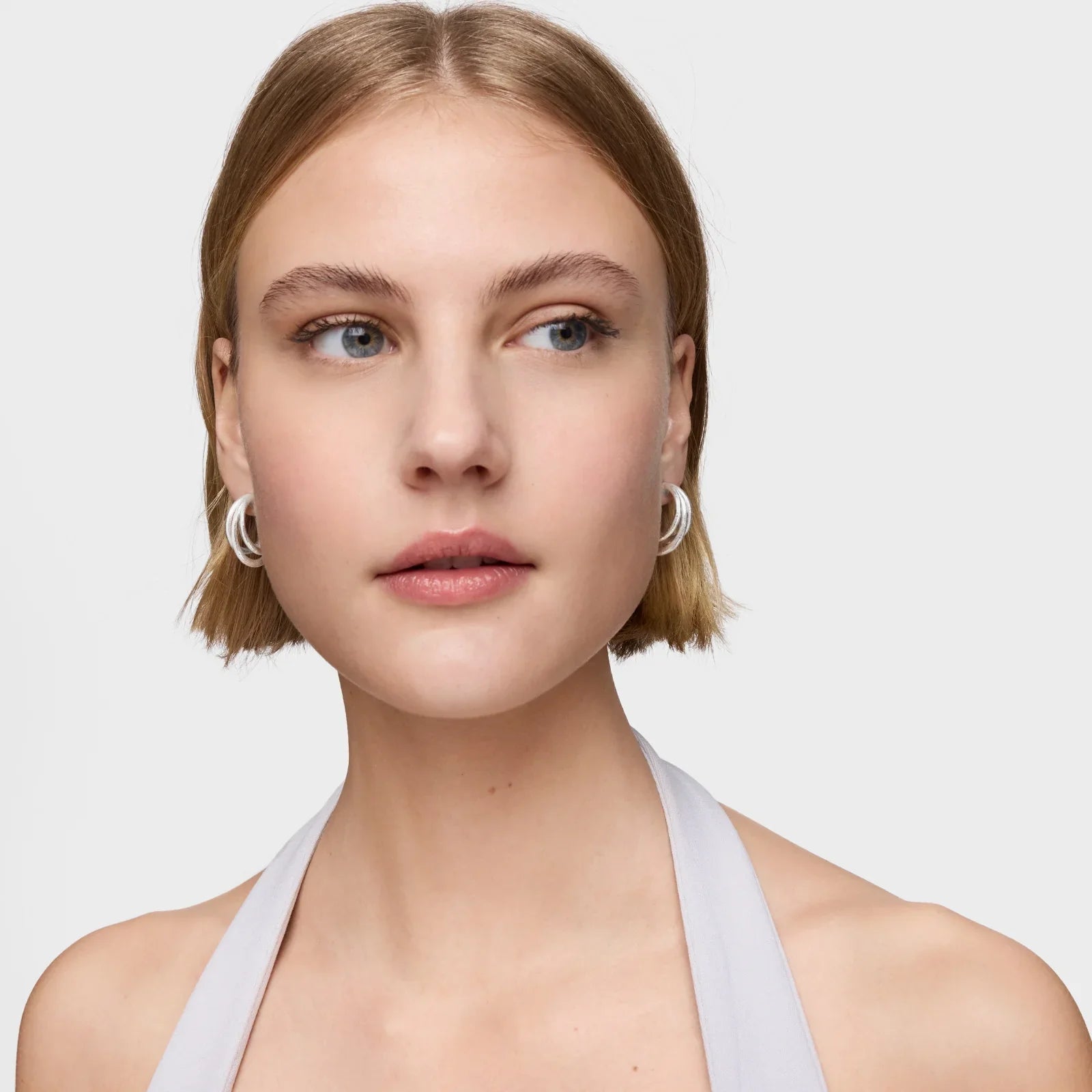 דוגמנית עונדת עגילי כסף עגולים, רקע לבן, צילום קמפיין CHOZEN מותגים מובילים