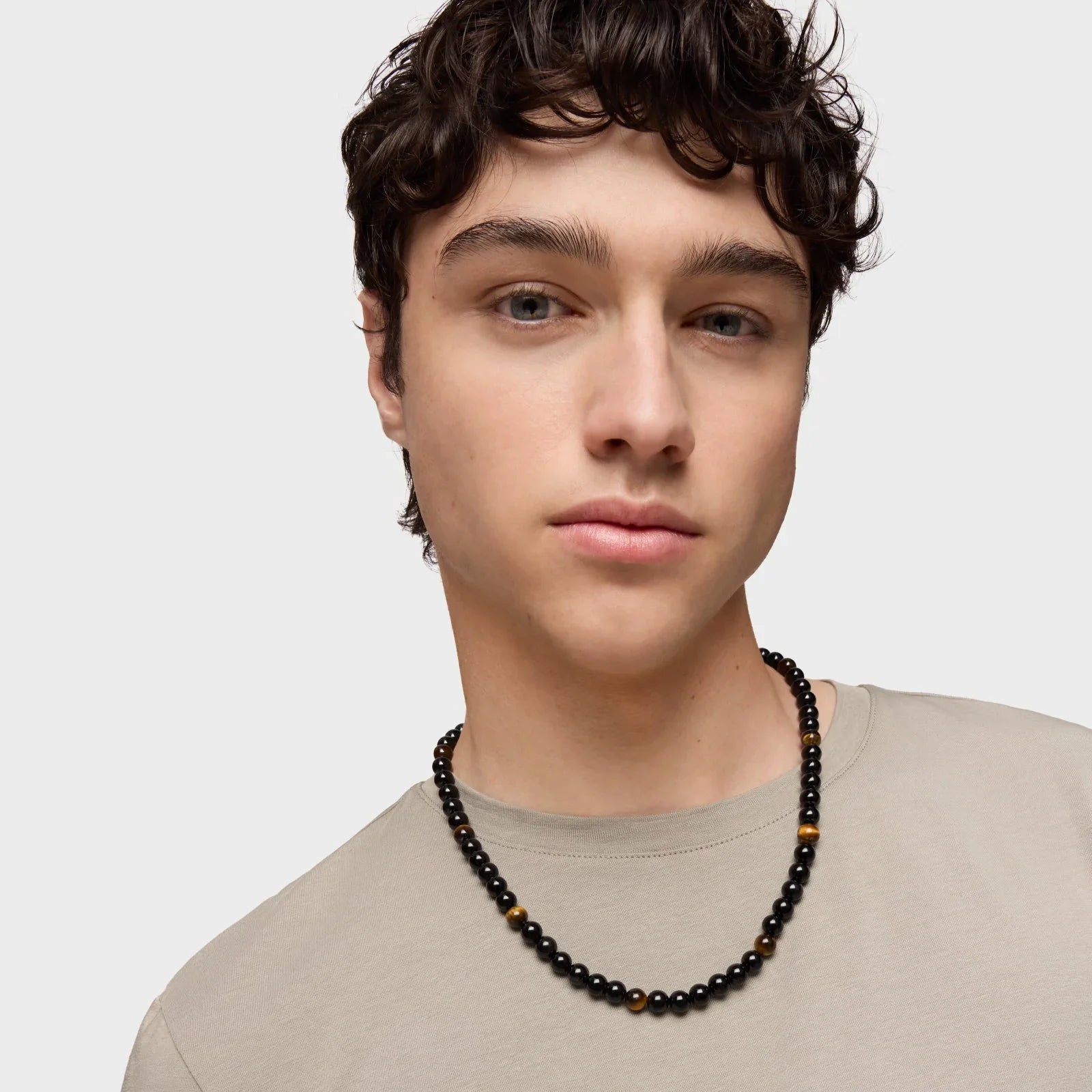 גבר צעיר עם שרשרת חרוזים שחורים, רקע אפור, צילום לאתר CHOZEN, אופנה לגבר