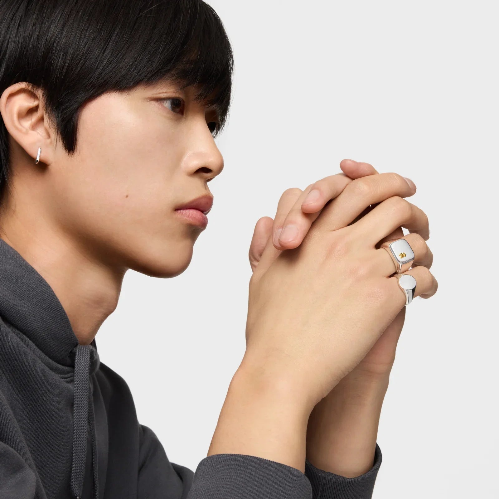 גבר צעיר עונד תכשיטים טרנדיים כסופים, טבעות ועגיל, על רקע לבן לאתר CHOZEN