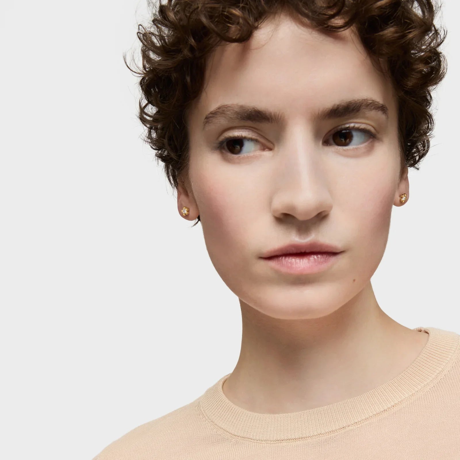 אישה עם שיער קצר עונד עגילים זהב עדינים, צילום תקריב לאופנת תכשיטים באתר CHOZEN