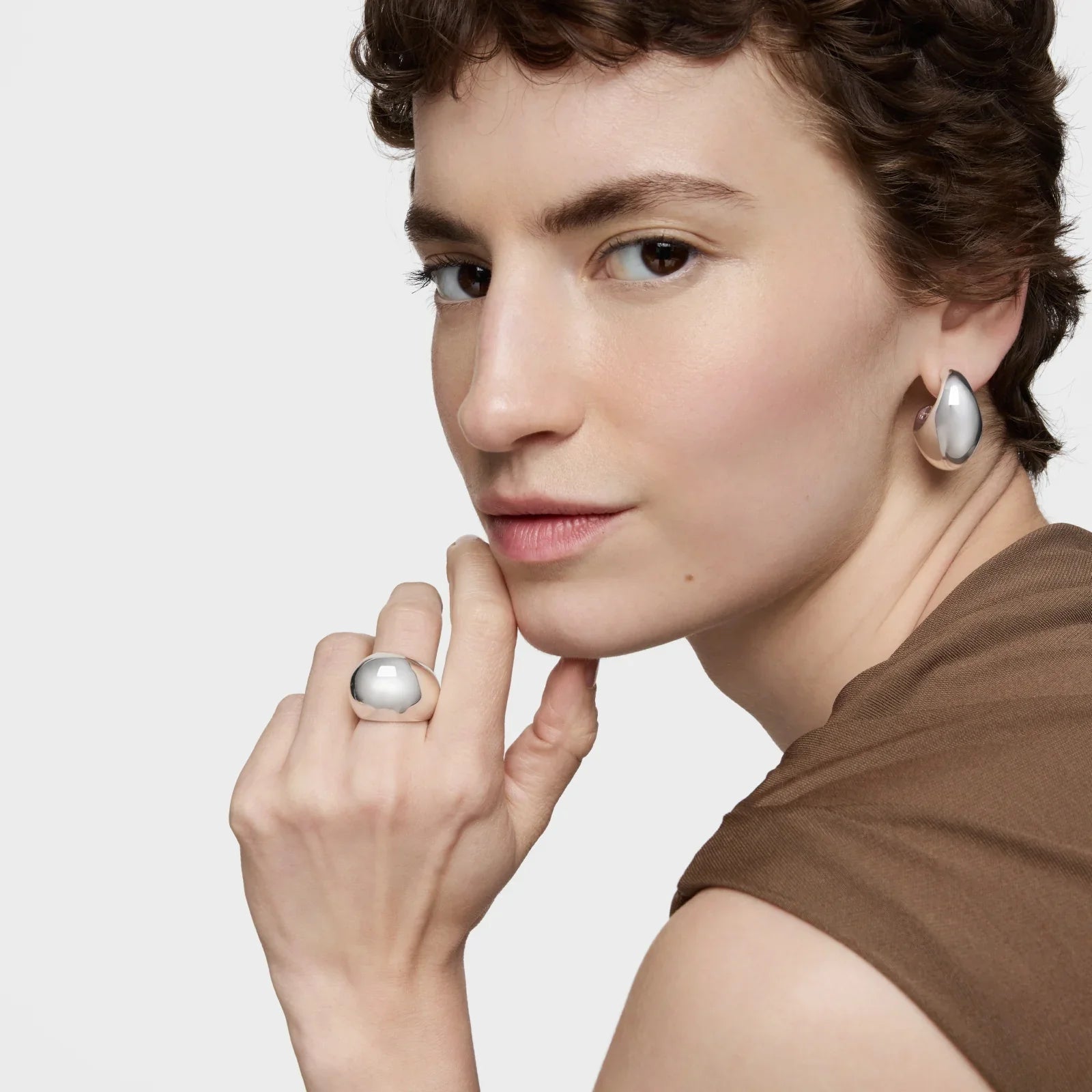 אישה עונדת עגילים וטבעת כסף בעיצוב מודרני, רקע בהיר, תכשיטים מבית CHOZEN