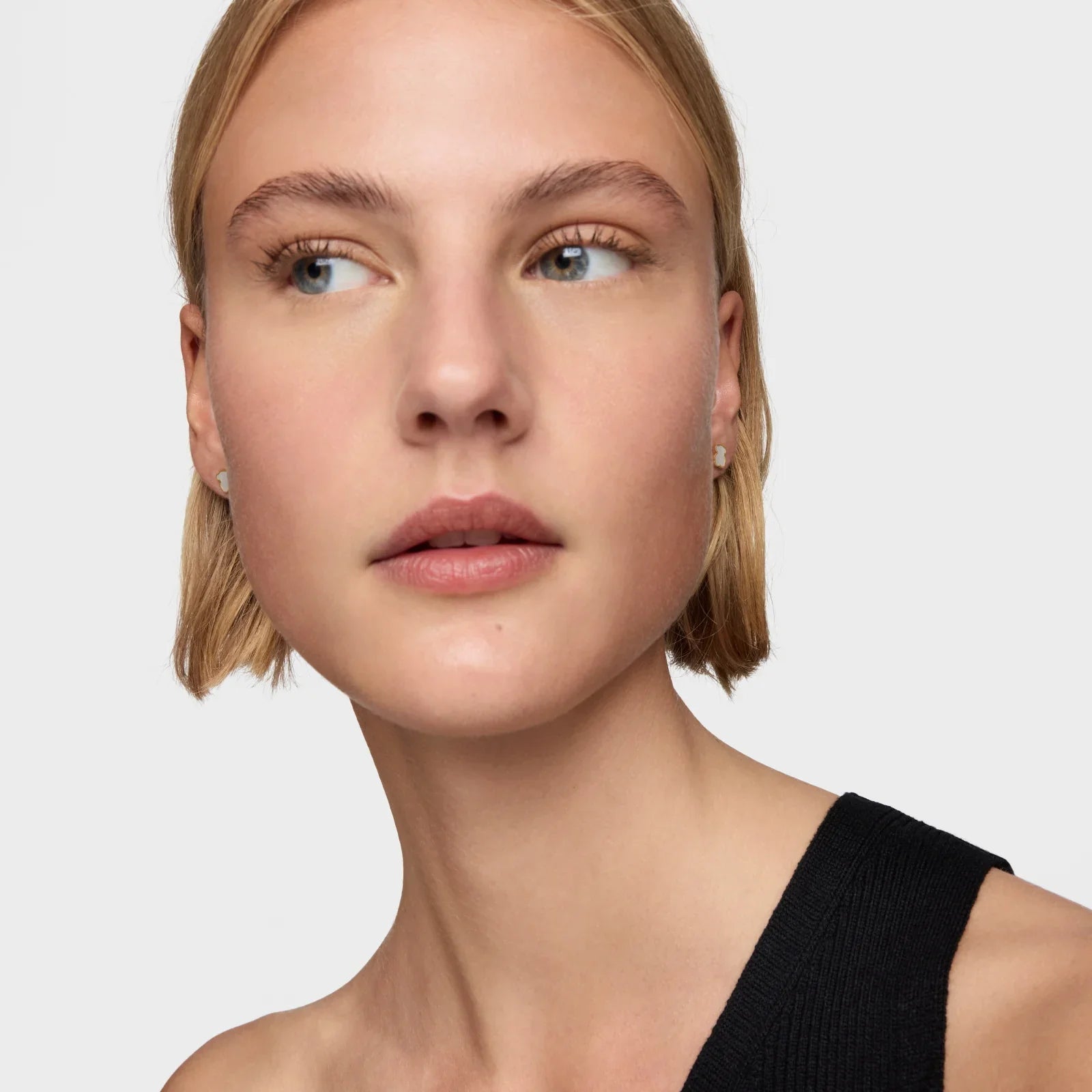 אישה עם שיער בלונד קצר, עגילי יהלום קטנים ולבוש שחור, על רקע לבן, מבית CHOZEN