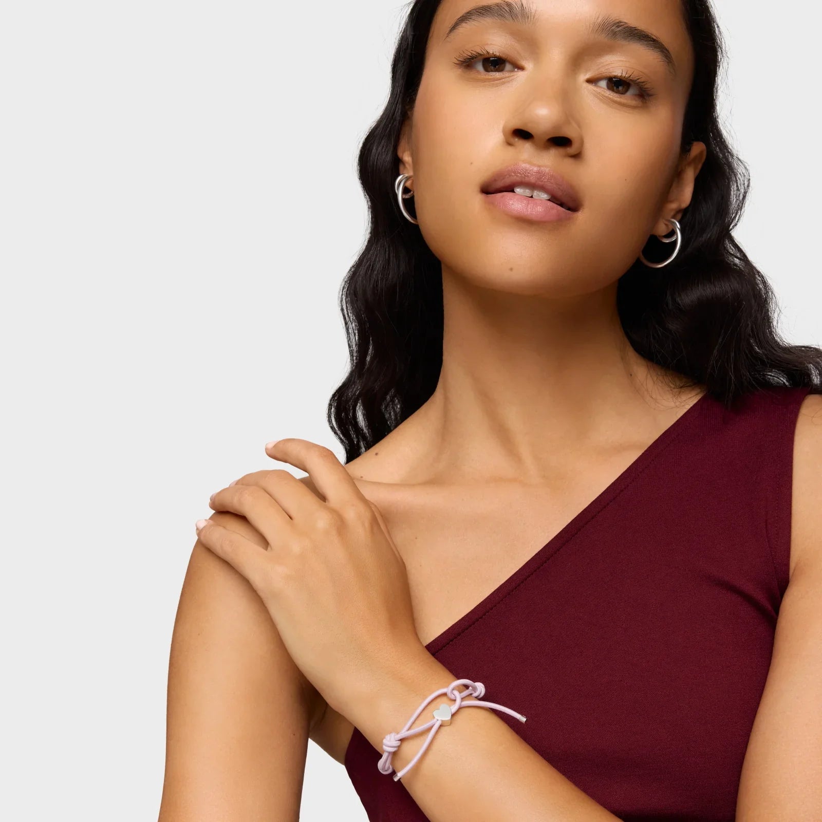 אישה עם חולצה בורדו, עונדת צמיד סגול ועגילי חישוק, מותגי תכשיטים מובילים ב-CHOZEN