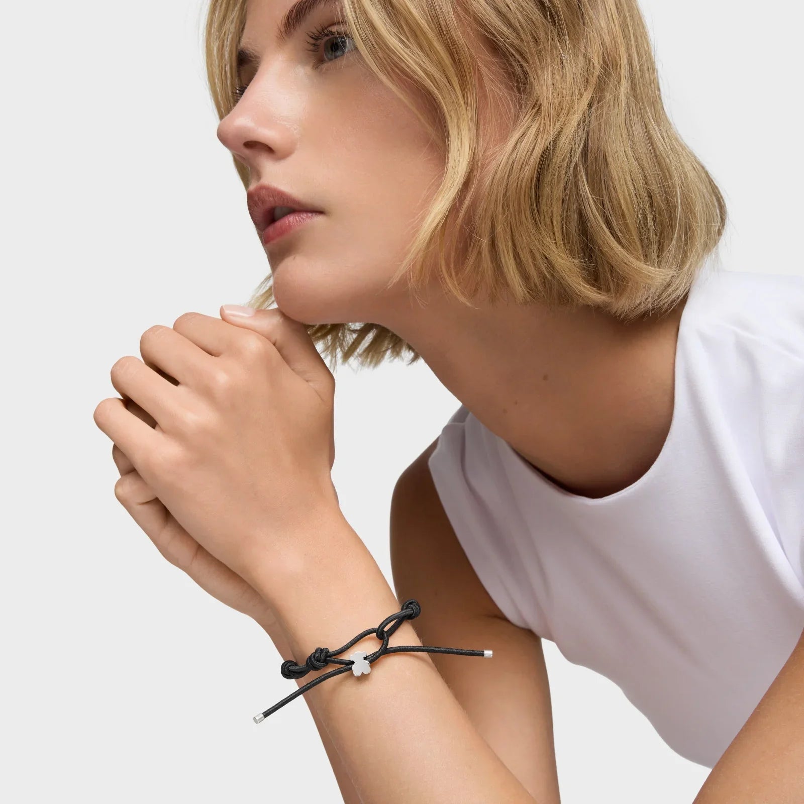 אישה עם שיער בלונדיני קצר לובשת צמיד אופנתי שחור עם תליון עדין, רקע חלק, תכשיטי CHOZEN מבית קבוצת אלפא