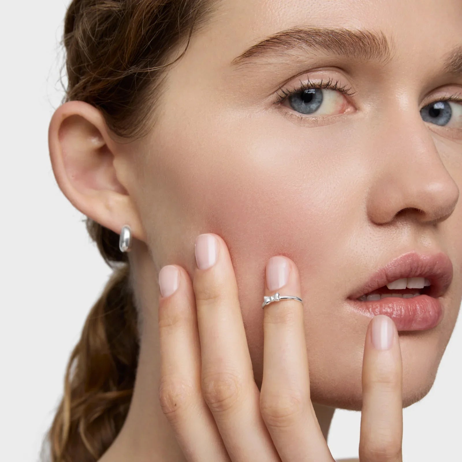 אישה עונדת עגיל כסף וטבעת עדינה על רקע בהיר, תכשיטי CHOZEN, ייבוא קבוצת אלפא