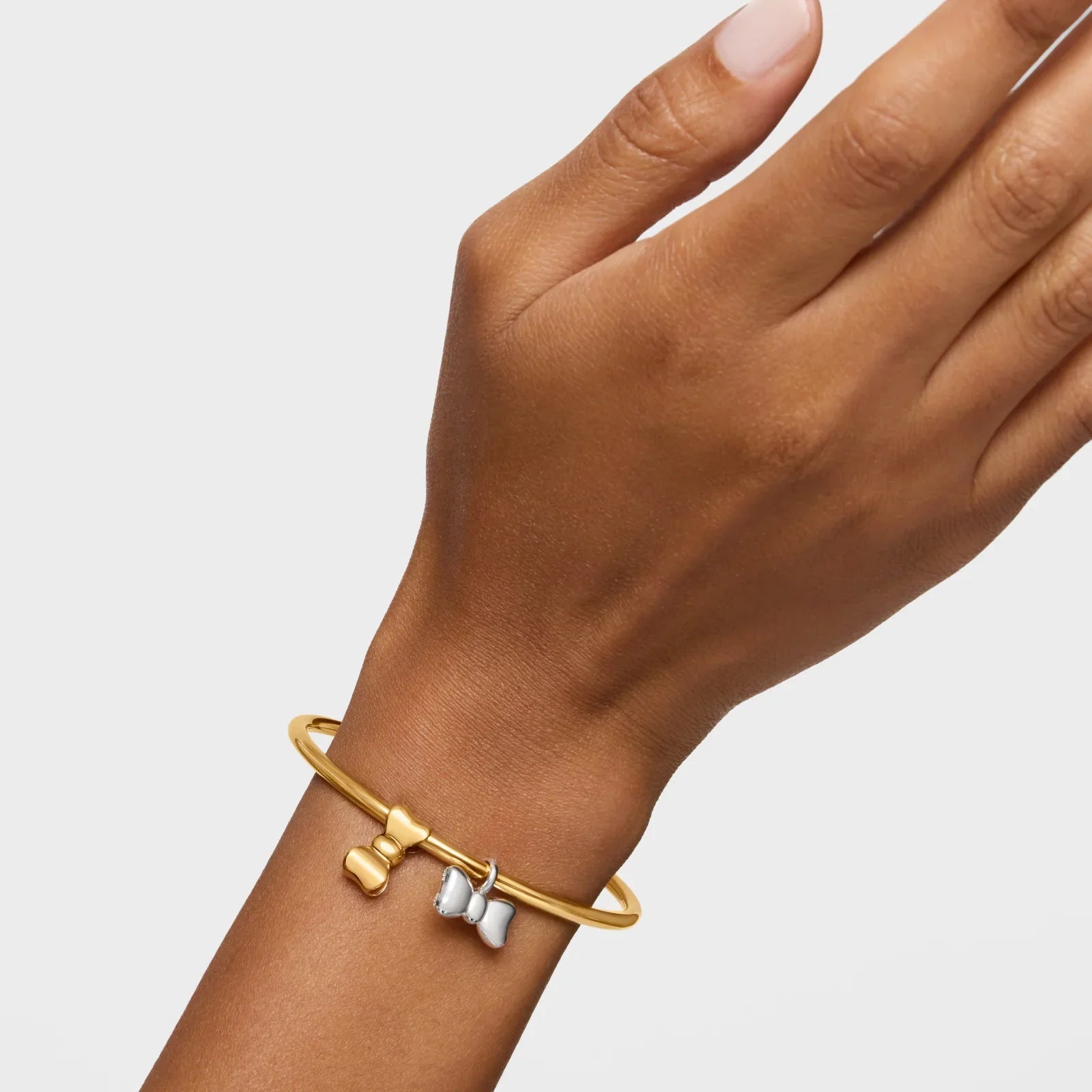 צמיד זהב פתוח עם תליון פרפר בצבע זהב ותליון פרפר כסוף על יד של אישה, מבית CHOZEN