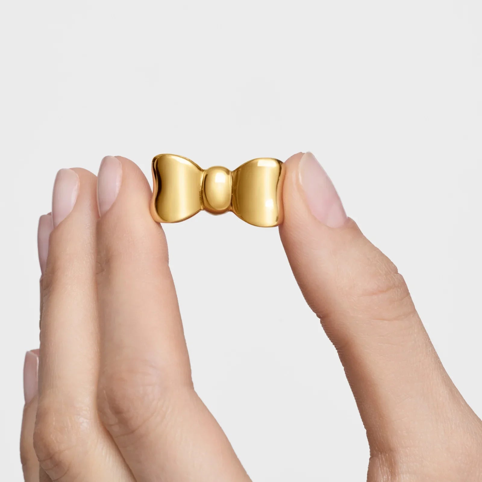 סיכת פפיון זהב בעיצוב יוקרתי של CHOZEN, מוחזקת בין אצבעות על רקע לבן