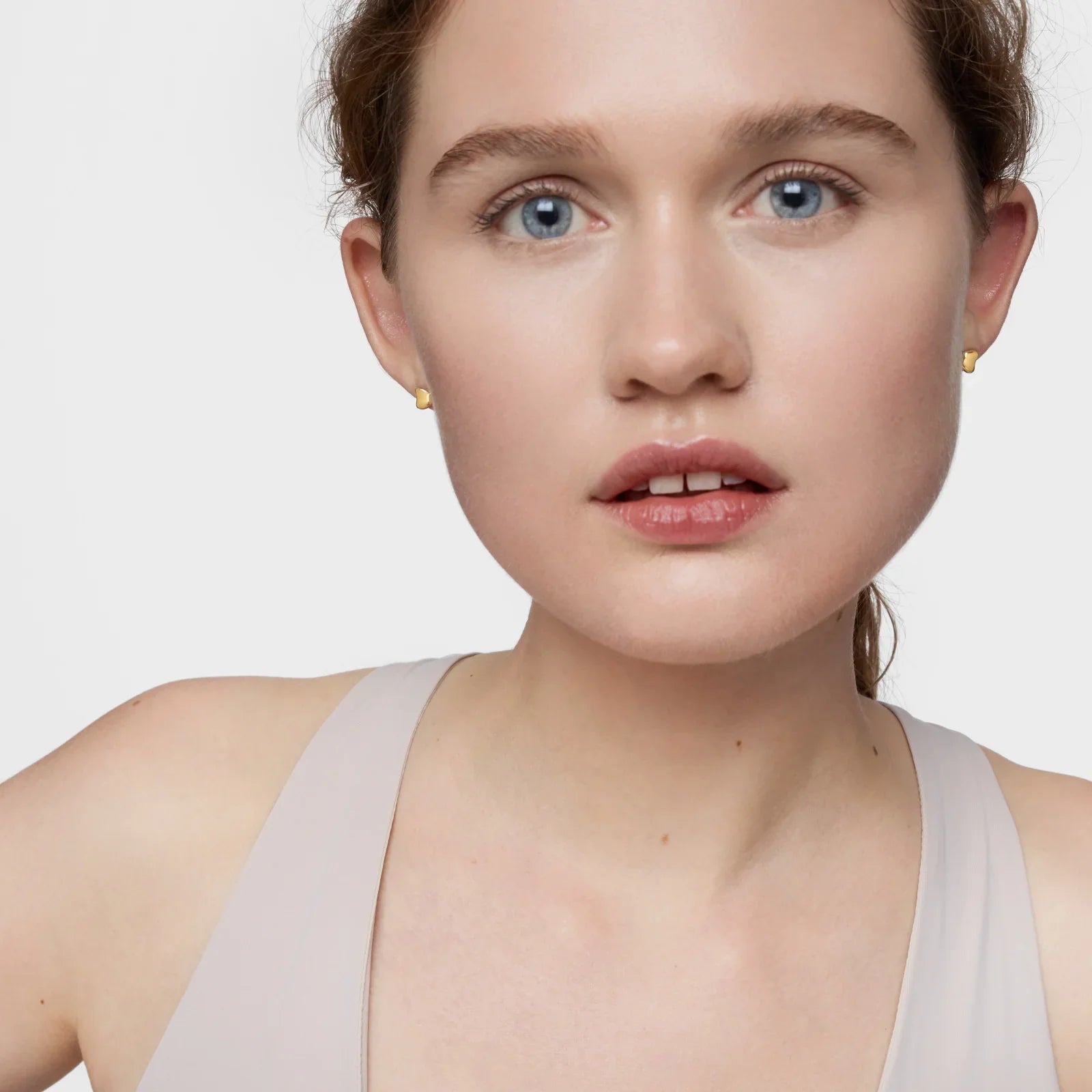 אישה עם עגילי זהב קטנים, רקע לבן, צילום תקריב לאתר CHOZEN מותגים מובילים