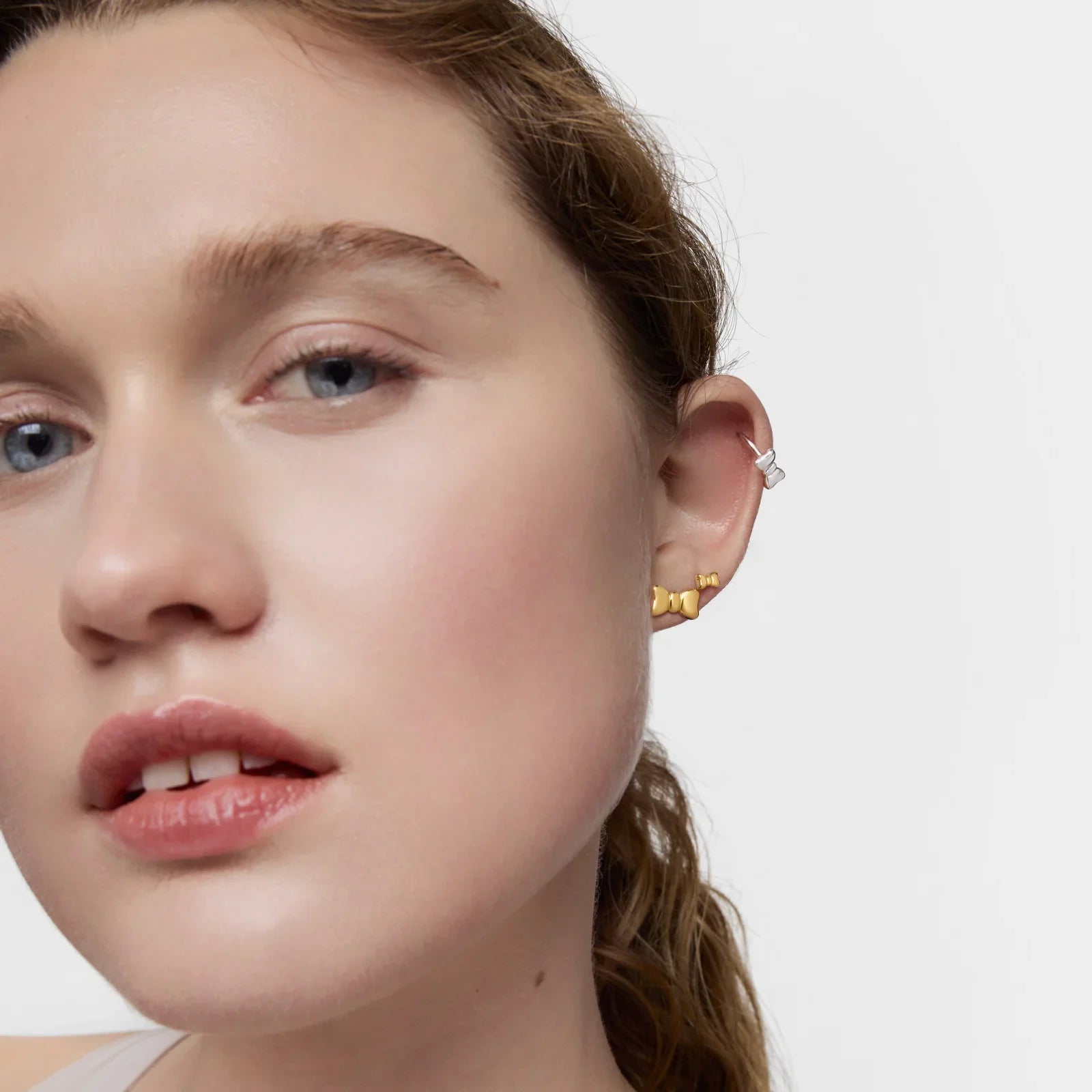 אישה עונדת עגילי זהב וכסף אופנתיים על רקע לבן, קולקציית תכשיטים CHOZEN מבית קבוצת אלפא