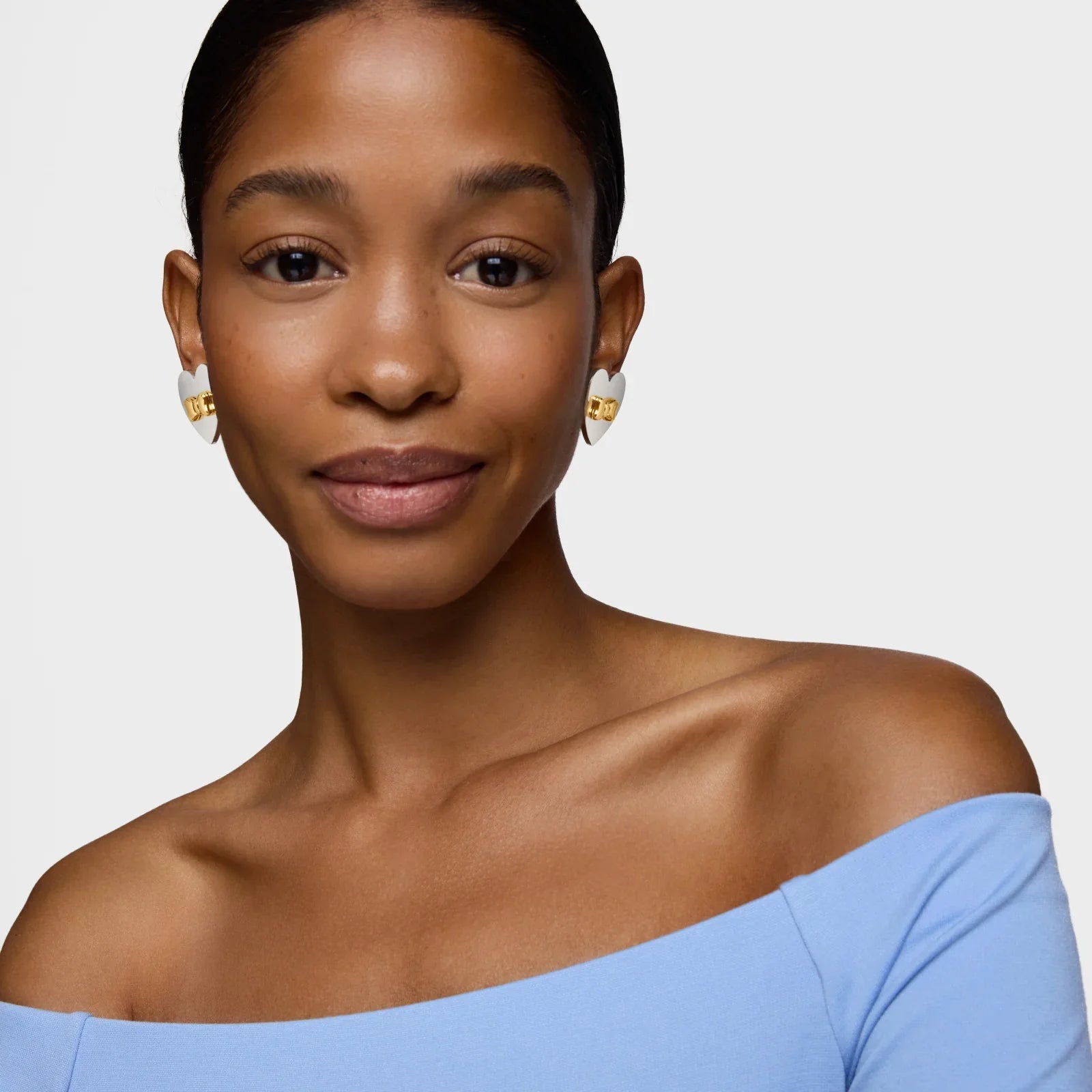 אישה עונדת עגילי לב זהב ולבן, לובשת חולצה כחולה, רקע לבן, מותגי יוקרה CHOZEN