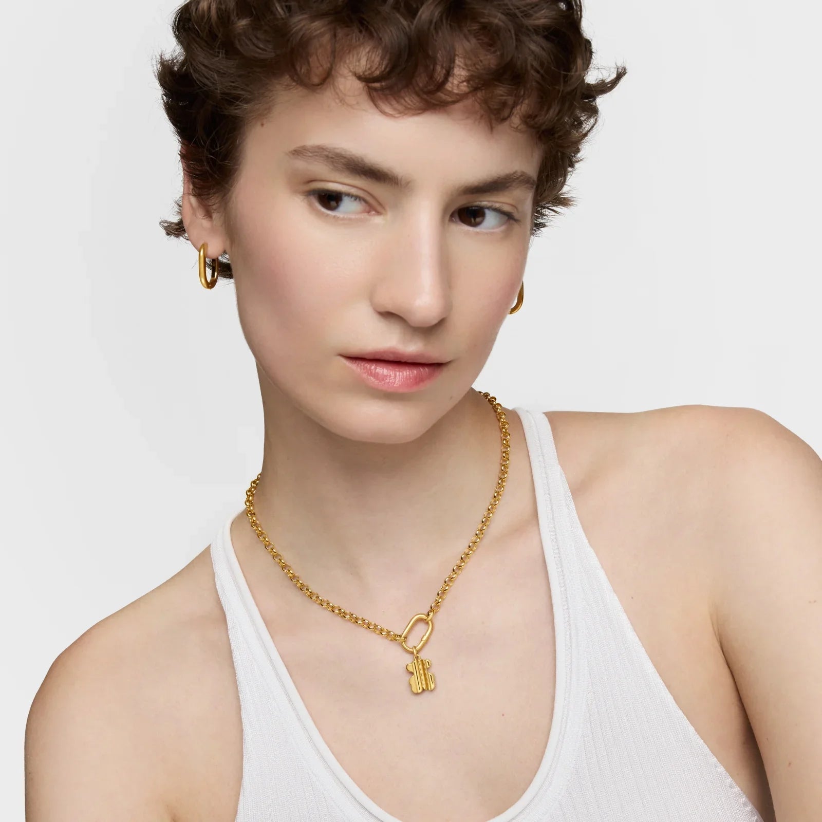 דוגמנית עם שרשרת חמסה זהב ועגילי חישוק, לבושה בגופיית לבן, CHOZEN מותגים מובילים