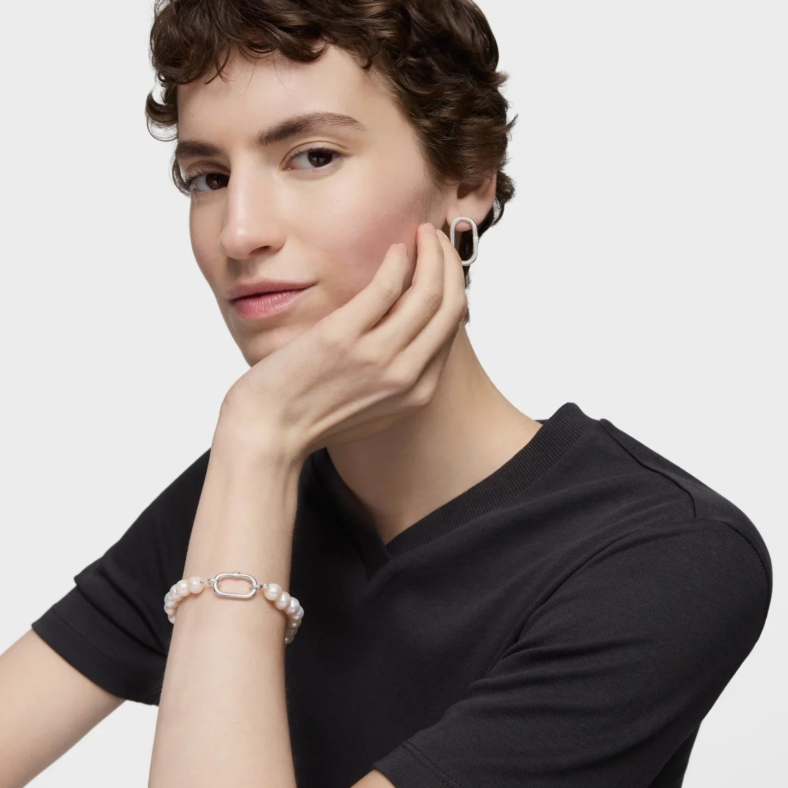 אישה עם שיער קצר לובשת חולצה שחורה, עונדת צמיד פנינים ועגיל מודרני, צילום לאתר CHOZEN