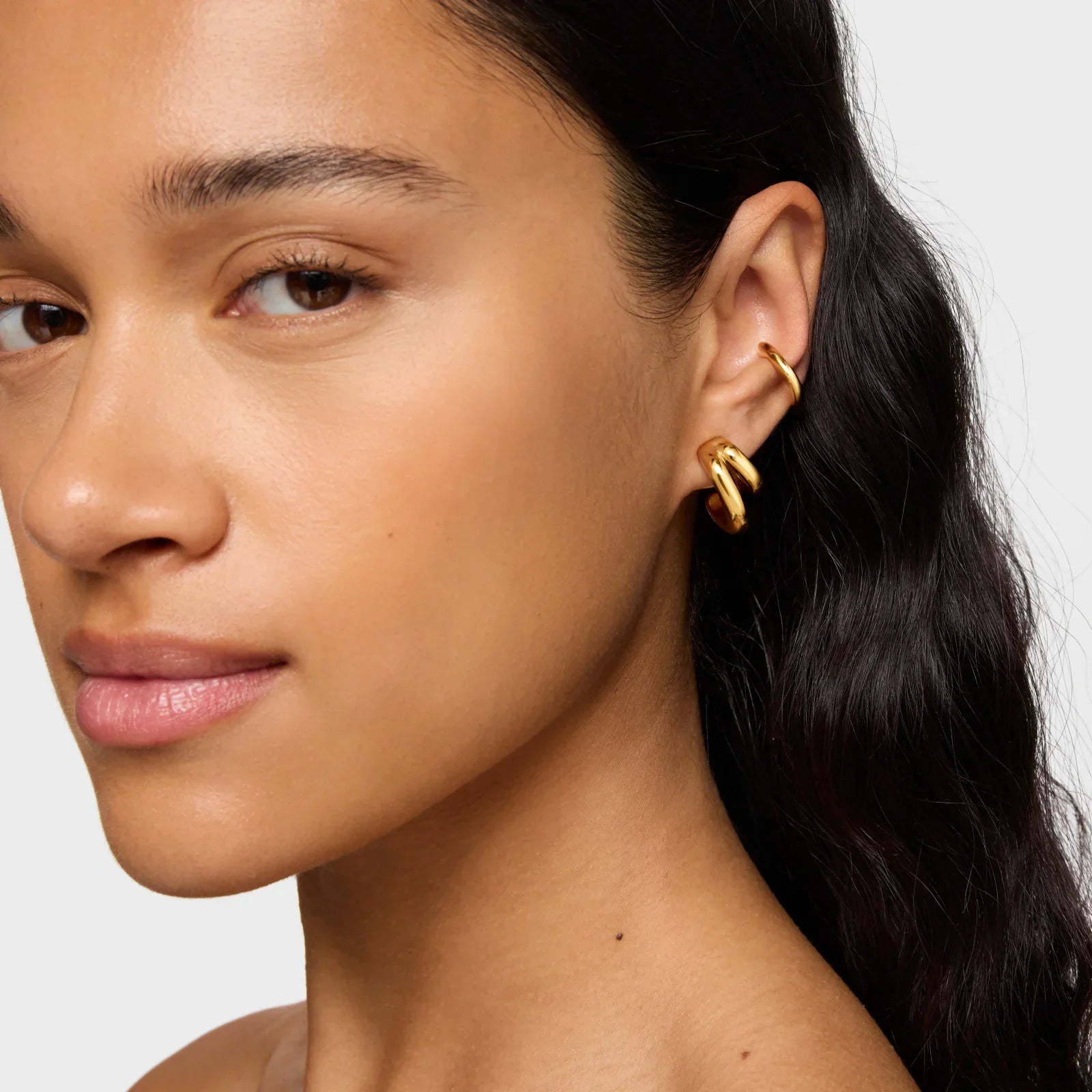 אישה עונדת עגילי זהב מעוצבים על רקע נייטרלי, תכשיטים אופנתיים CHOZEN