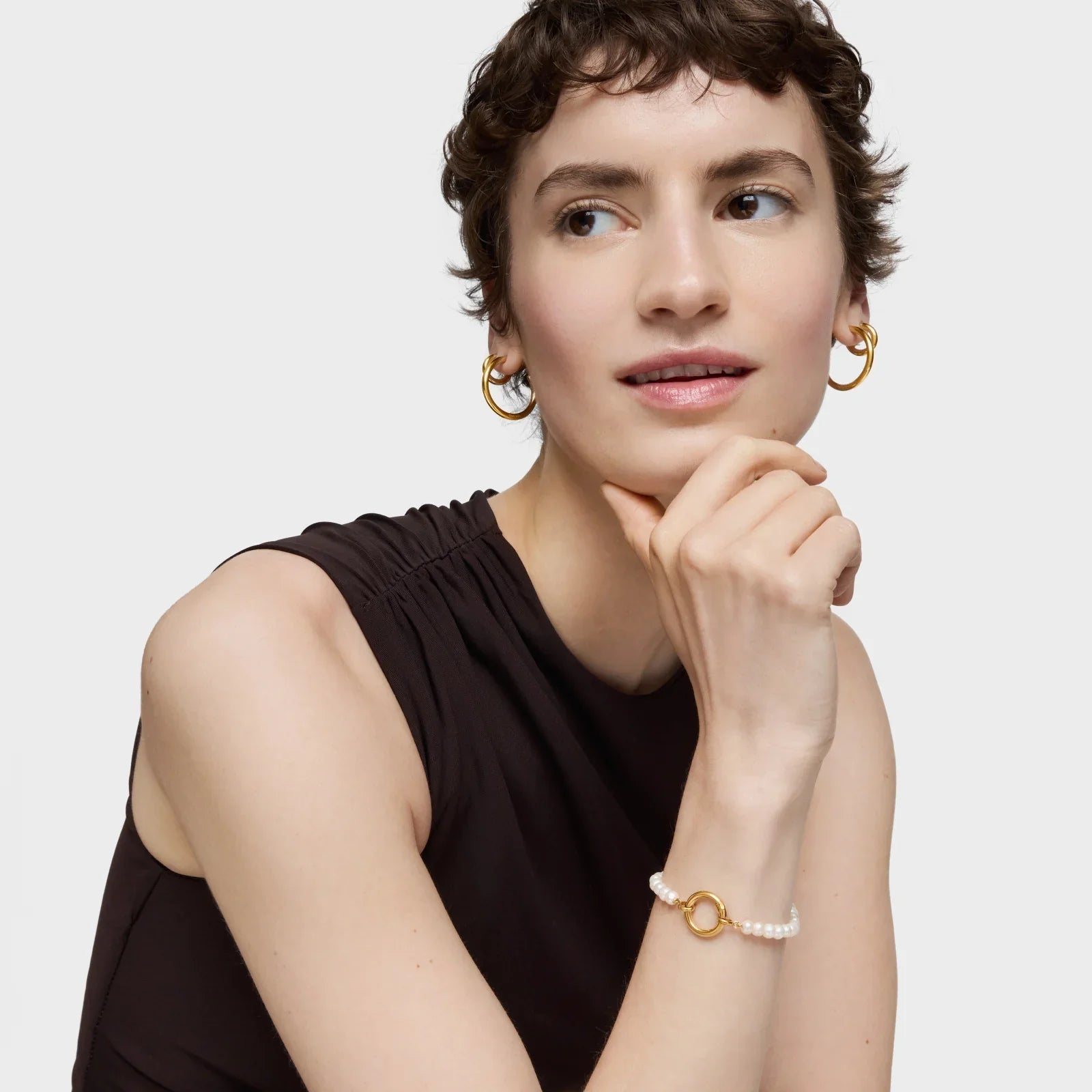 אישה עונדת עגילי זהב וצמיד פנינים אופנתי, לבושה בגופיה שחורה, צילום קידום CHOZEN