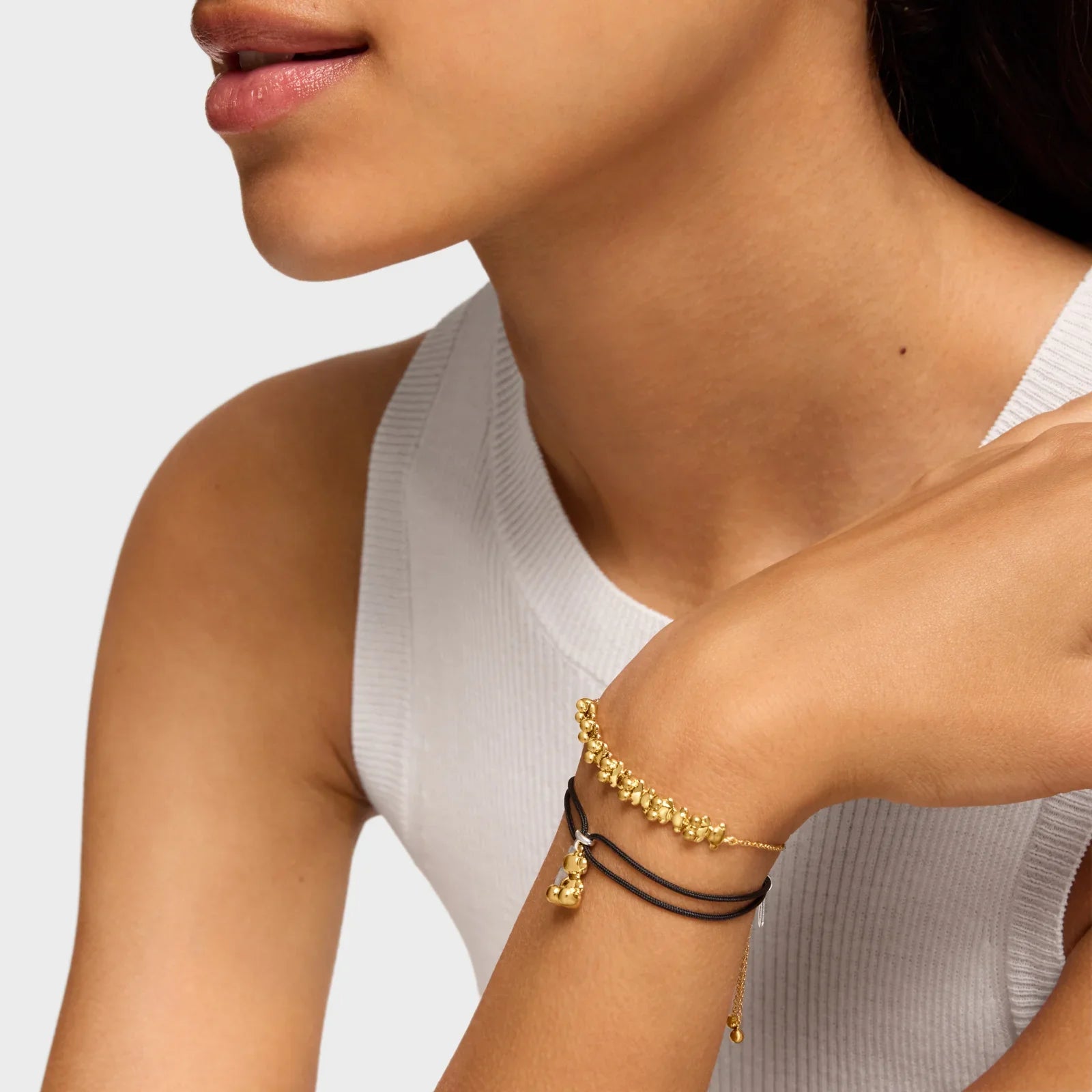 צמידים מזהב על יד אישה, עיצוב יוקרתי, מותג CHOZEN, גופייה לבנה, צילום תקריב