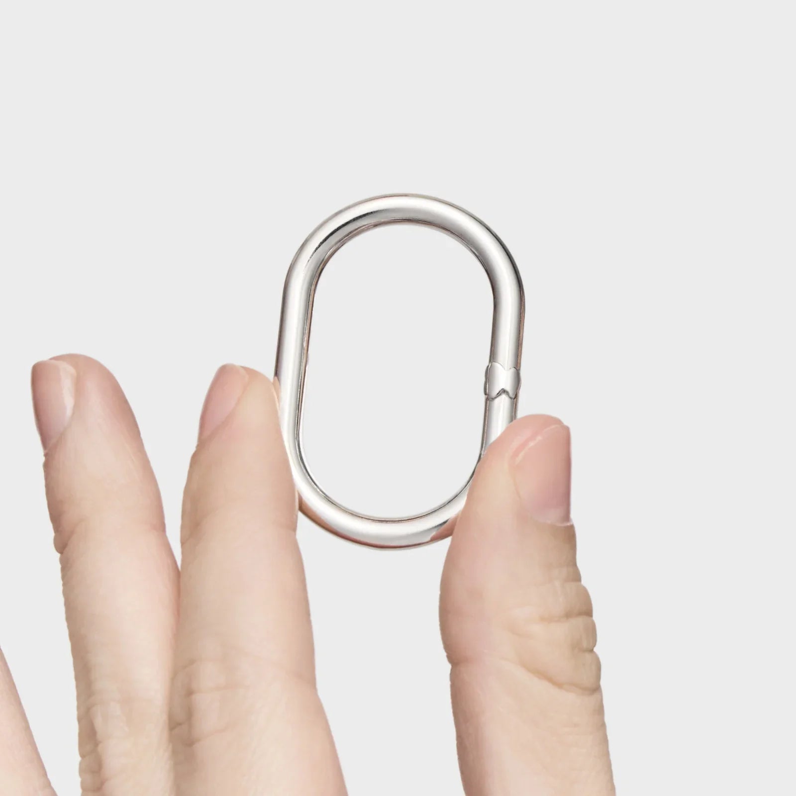 קרבינר מתכת כסוף בעיצוב מודרני מוחזק בין אצבעות, מוצר CHOZEN, קבוצה אלפא