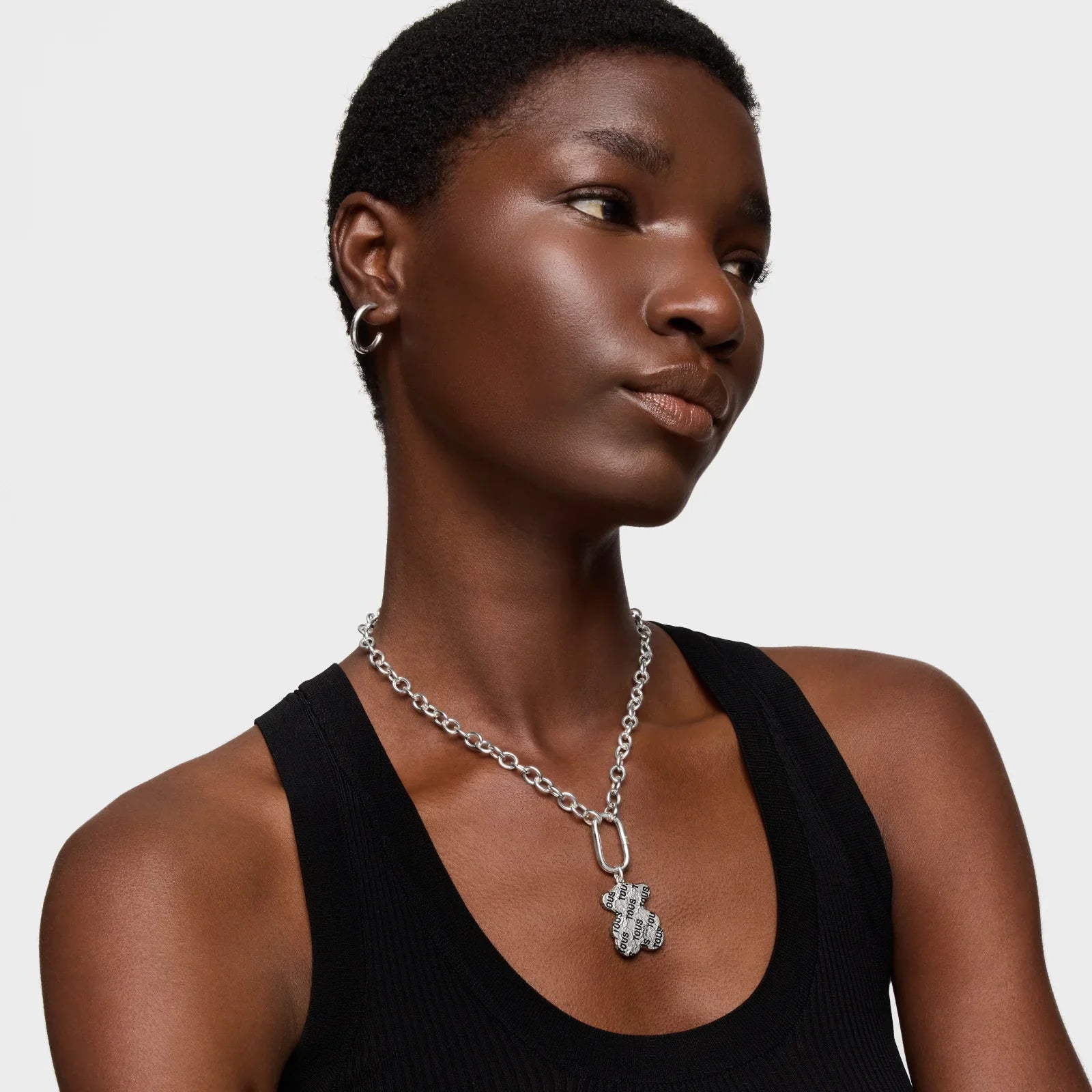 דוגמנית עונדת שרשרת כסף בעיצוב ייחודי, עגילי חישוק, חולצה שחורה על רקע לבן, אופנת CHOZEN