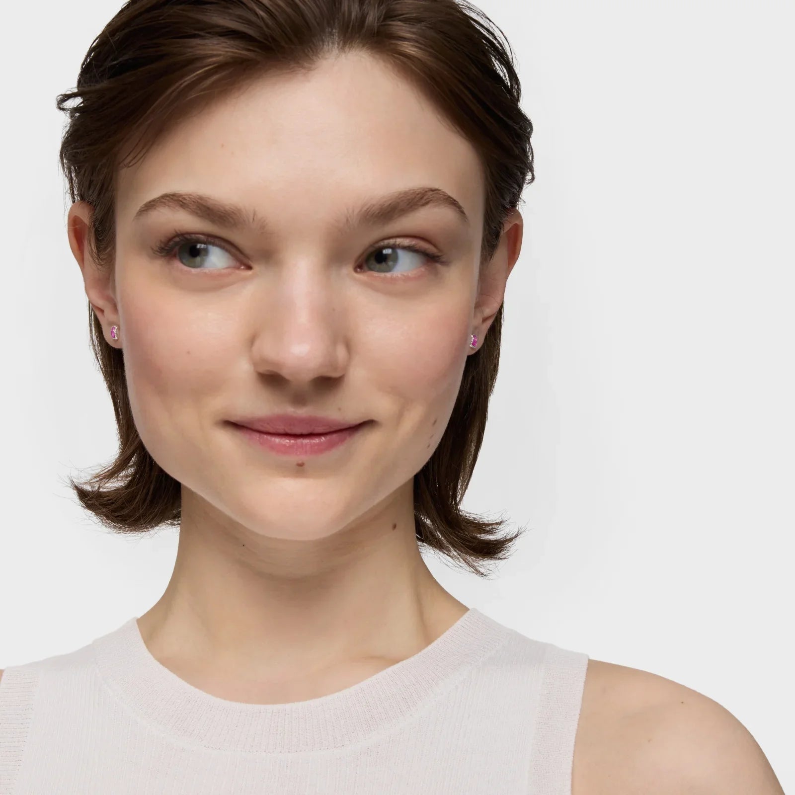 אישה עונדת עגילי יוקרה קטנים ורודים, צילום תקריב לאתר המותגים CHOZEN