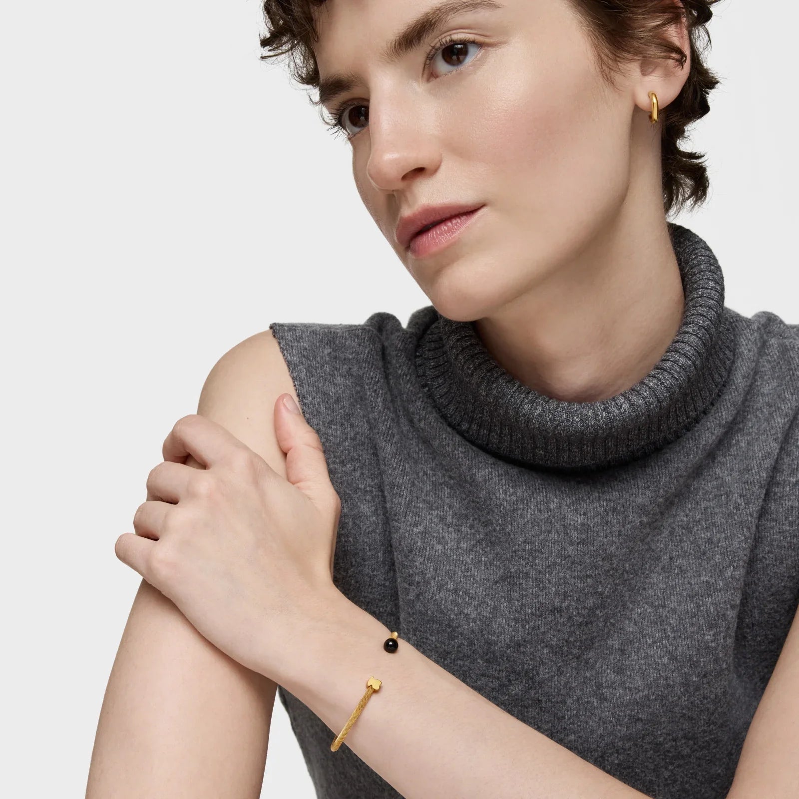 אישה עם טופ אפור, עונדת עגיל זהב וצמיד זהב בעיצוב מודרני מאוסף CHOZEN