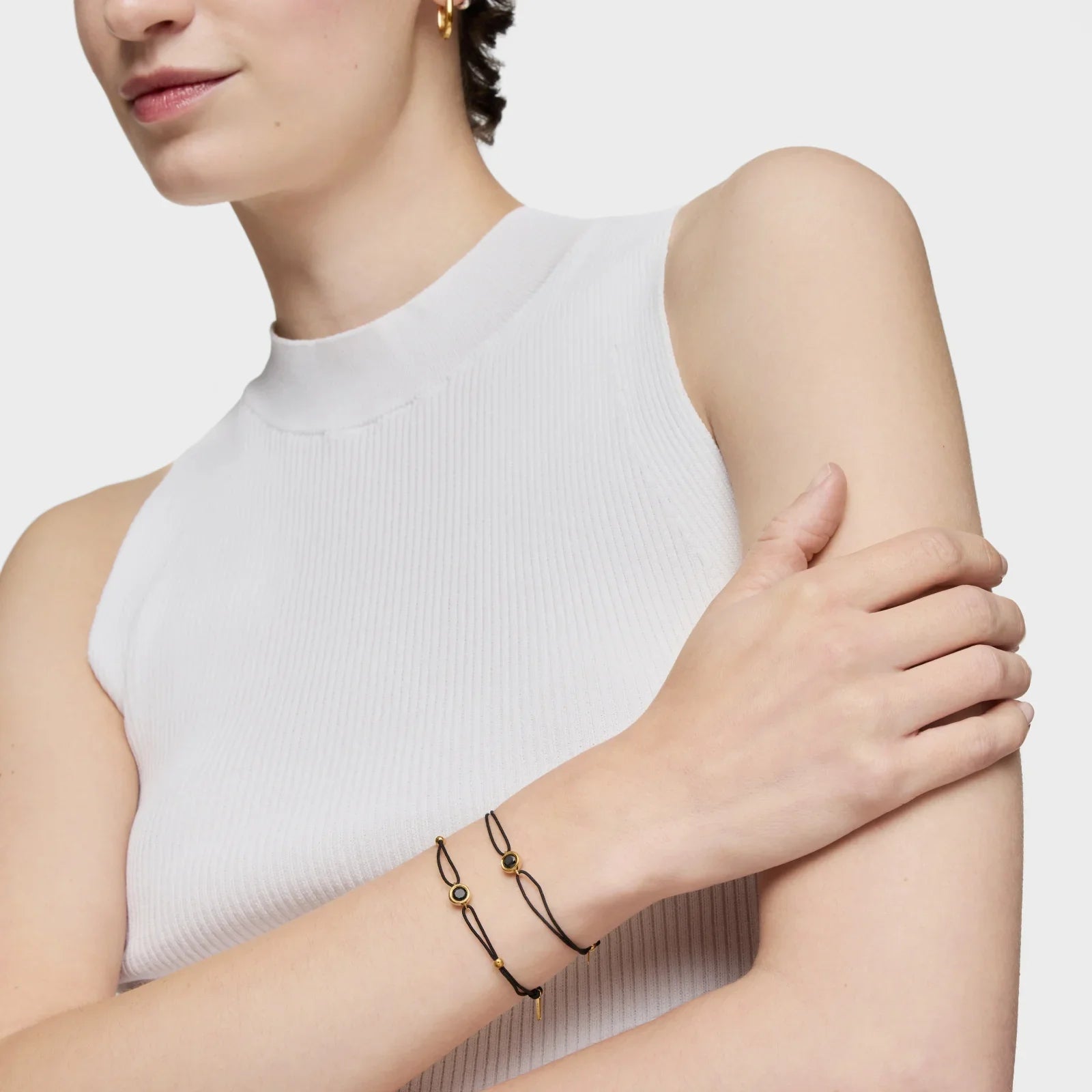 אישה עונדת שני צמידים דקים בעיצוב מודרני בצבע שחור וזהב, על רקע לבן, CHOZEN מותגים מובילים