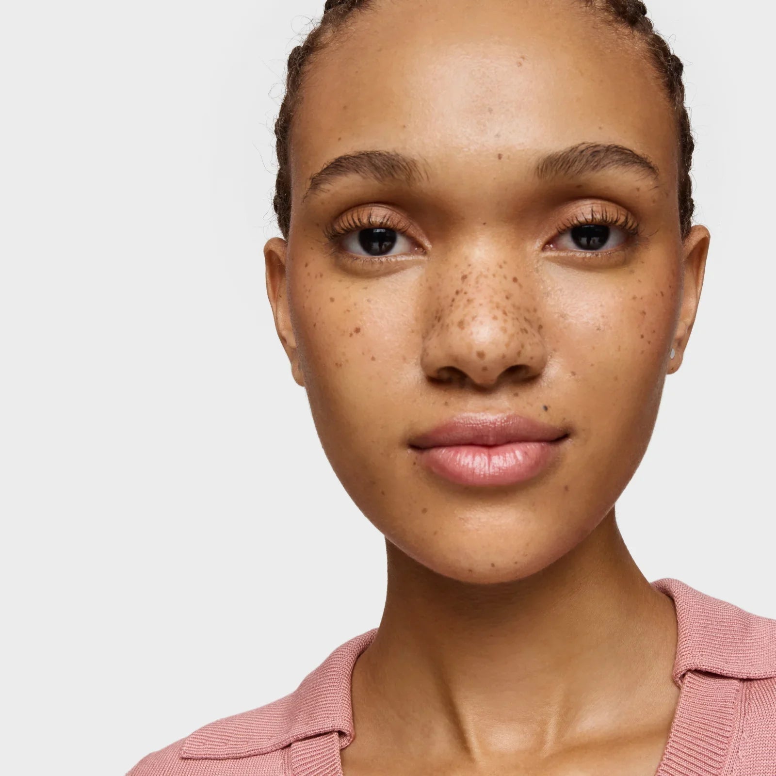 דיוקן מקרוב של אישה צעירה עם נמשים, עם עור טבעי, לבושה בחולצה ורודה, רקע לבן - מותגי יופי CHOZEN