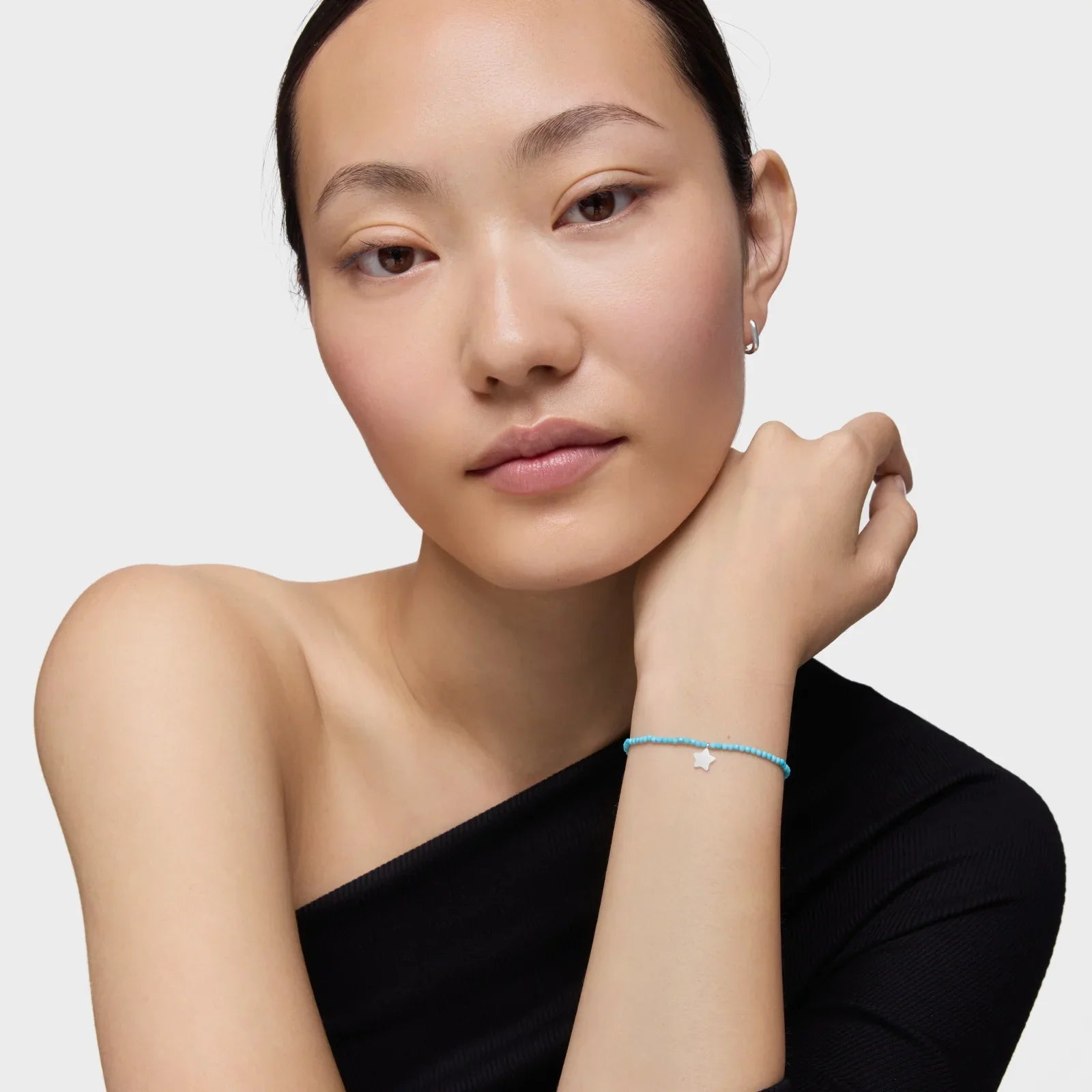 דוגמנית עונדת צמיד חרוזים טורקיז עם תליון כוכב כסף, רקע בהיר, CHOZEN תכשיטים אופנתיים