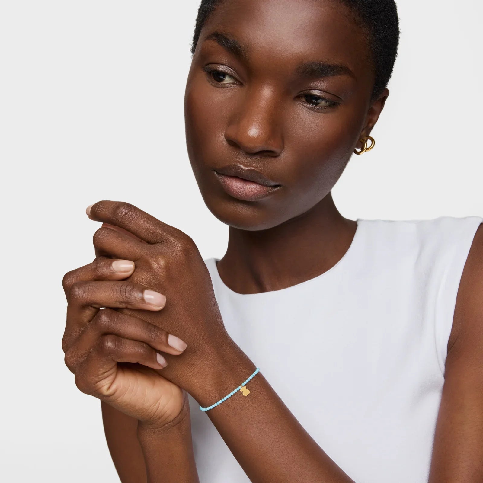 אישה עונדת צמיד עדין עם תליון זהב בחולצה לבנה, תכשיטים מבית CHOZEN מותגים מובילים