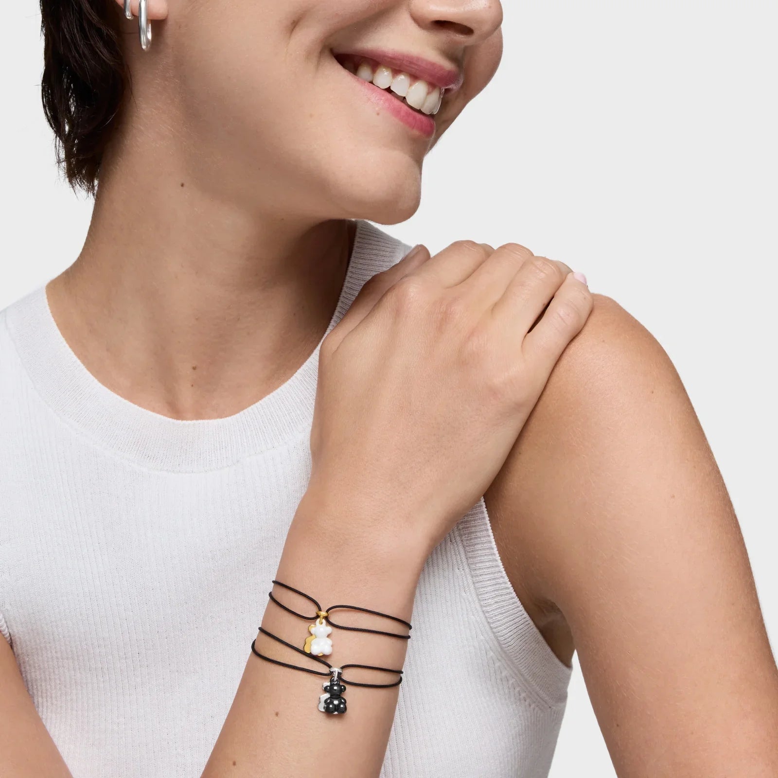 אישה עונדת צמידי חוט שחור עם תליון דובי כסף וזהב, צילום תקריב ליד על רקע בהיר מ-CHOZEN