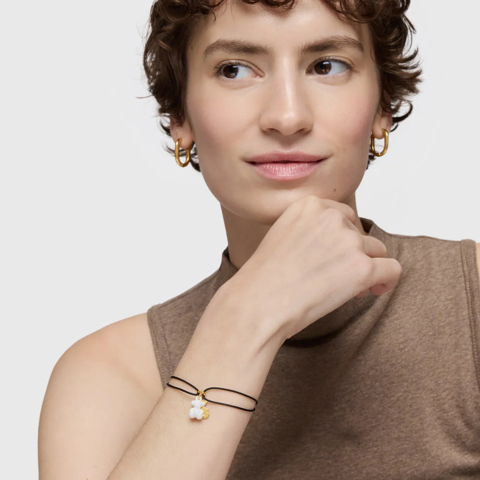 אישה עונדת צמיד אלגנטי עם תליון פרח לבן ותכשיטי זהב, מצולמת לאתר CHOZEN