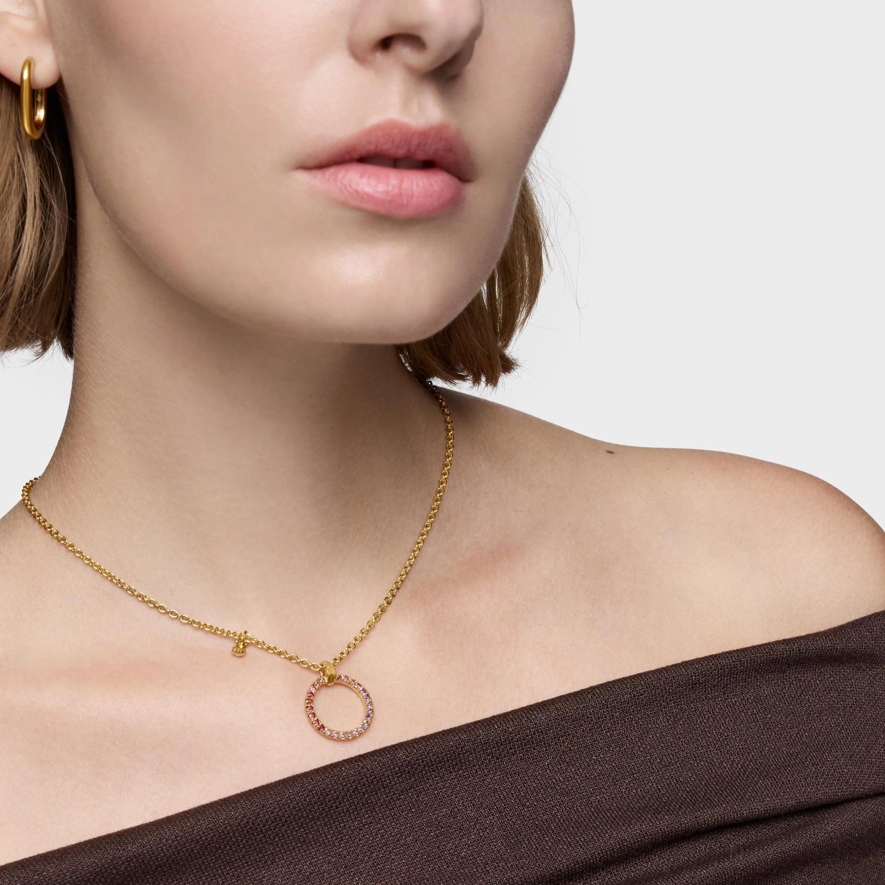 שרשרת זהב עדינה עם תליון עיגול משובץ אבנים צבעוניות על צוואר של אישה